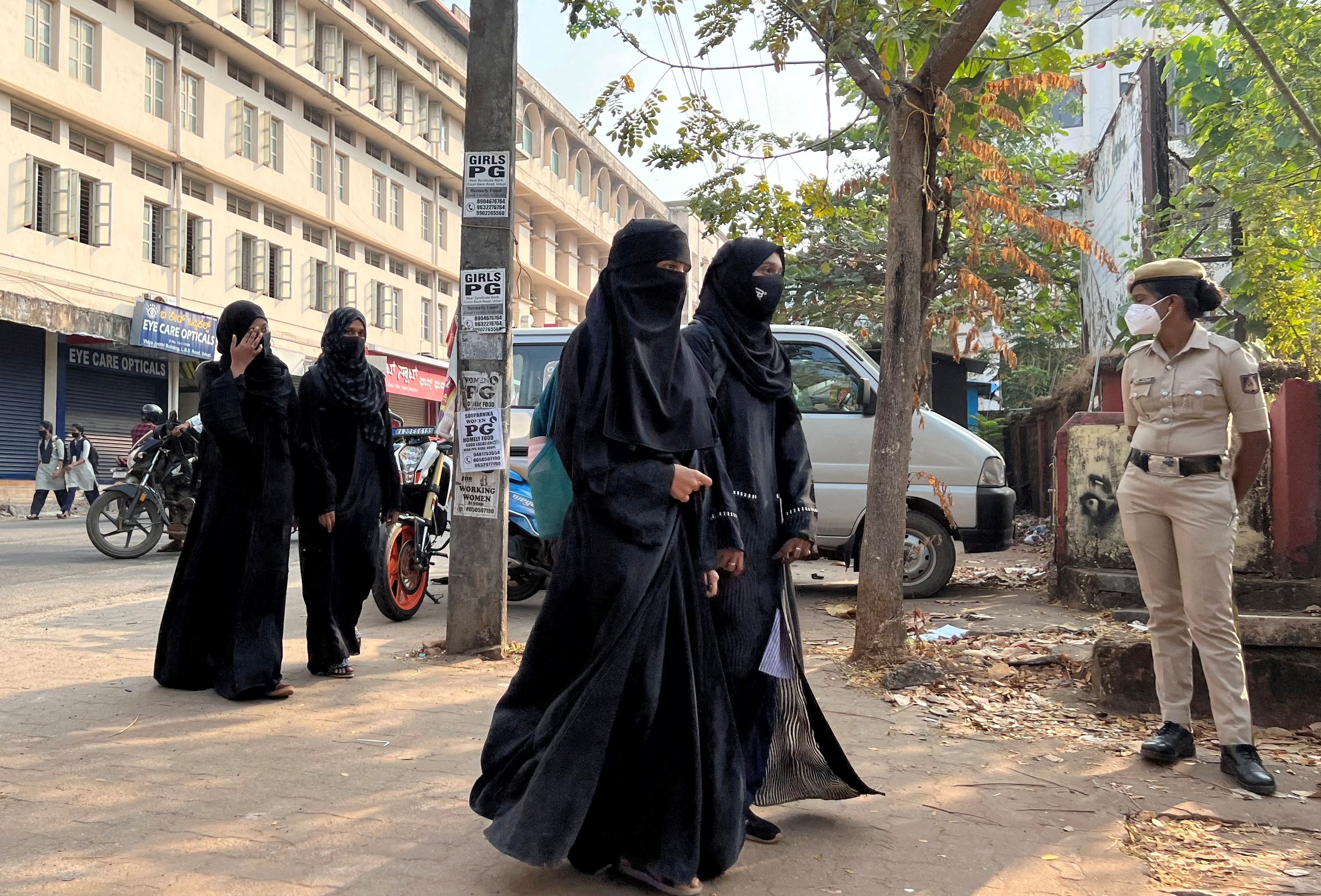 Hijab wearing schoolgirls arrive to attend their classes as a policewoman stands guard at a government girls school in Udupi town