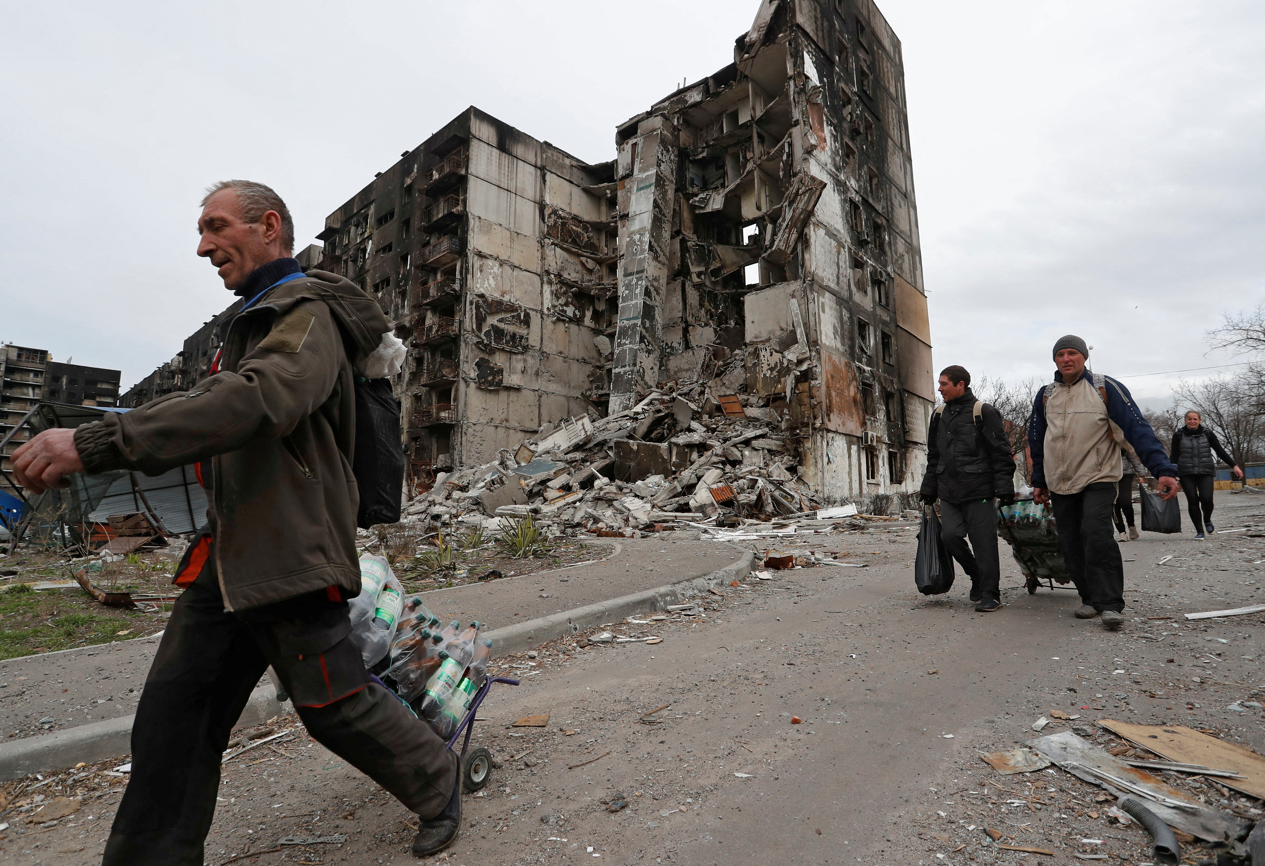 Local residents walk past a destroyed building in Mariupol