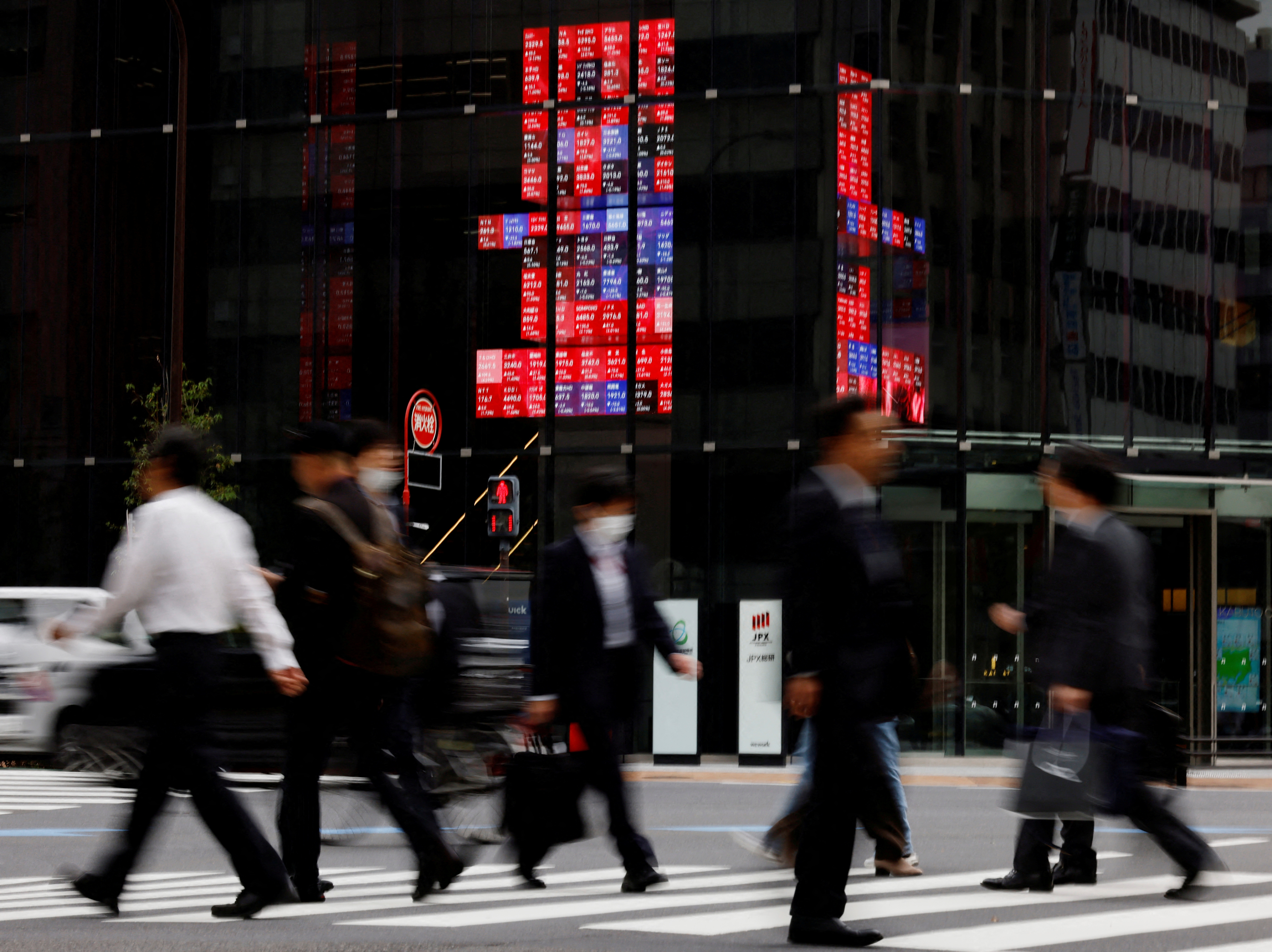 Pedestrians walk past an electronic board displaying various companies' share prices, at a business district in Tokyo