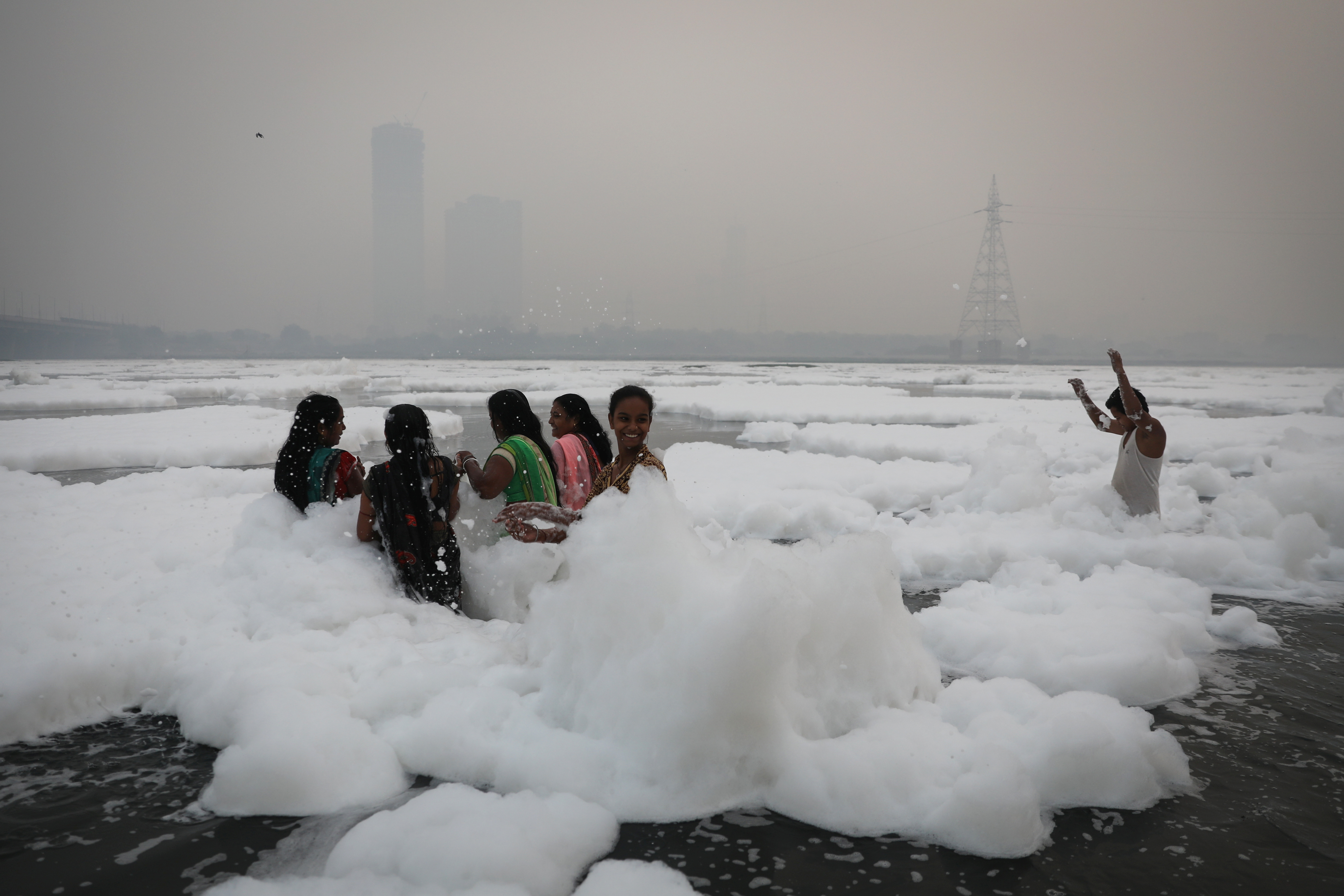 People bathe amidst the foam covering the polluted Yamuna river on a smoggy morning in New Delhi, India November 8, 2021. REUTERS/Anushree Fadnavis