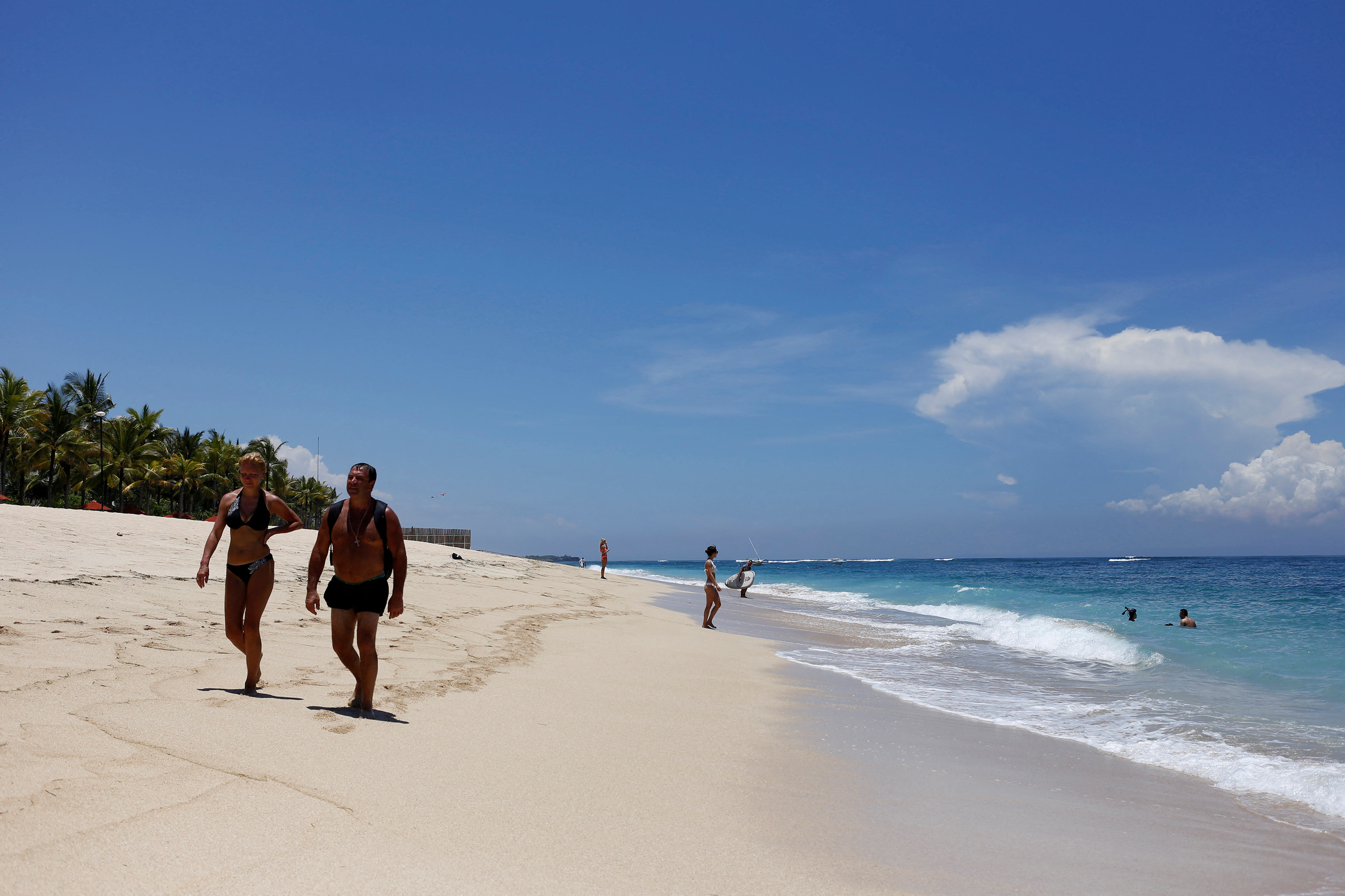 Tourists walk along a beach in the luxury resort area of Nusa Dua