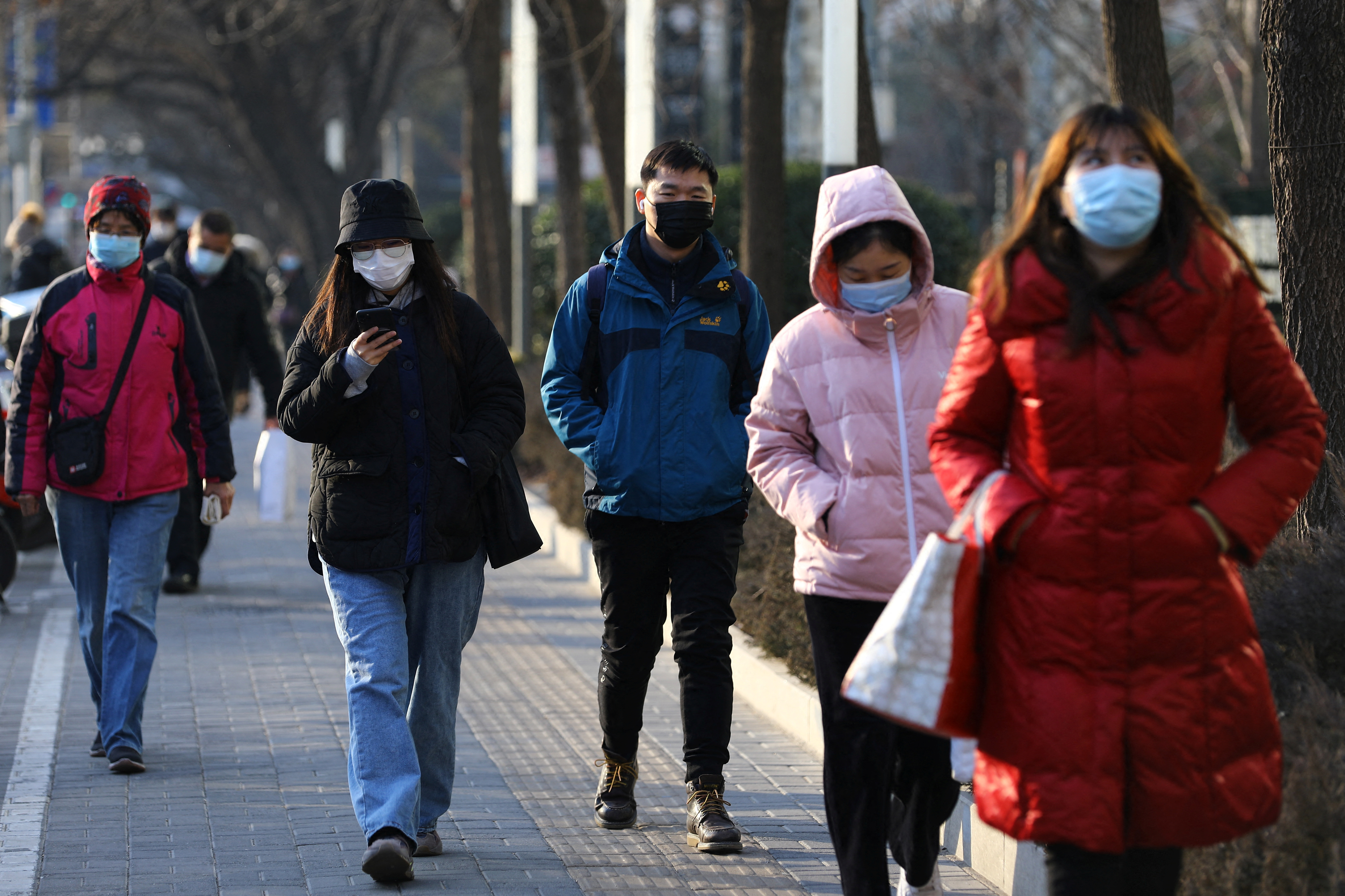 People wearing protective face masks walk on a street during morning rush hour as the COVID-19 pandemic continues in the country, in Beijing