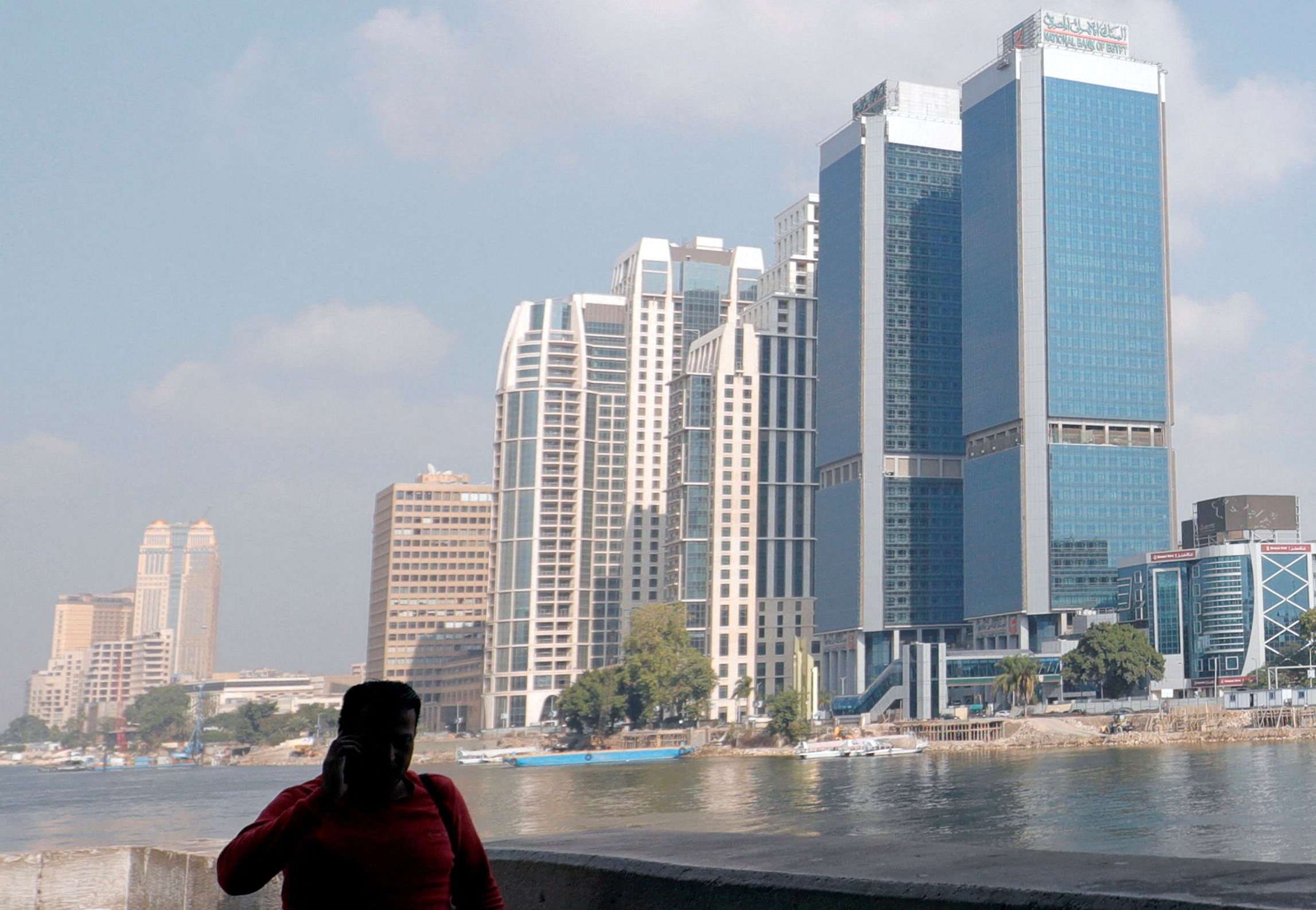 A man walks along the bank of the Nile river in front of high towers of hotels, banks and office buildings in Cairo