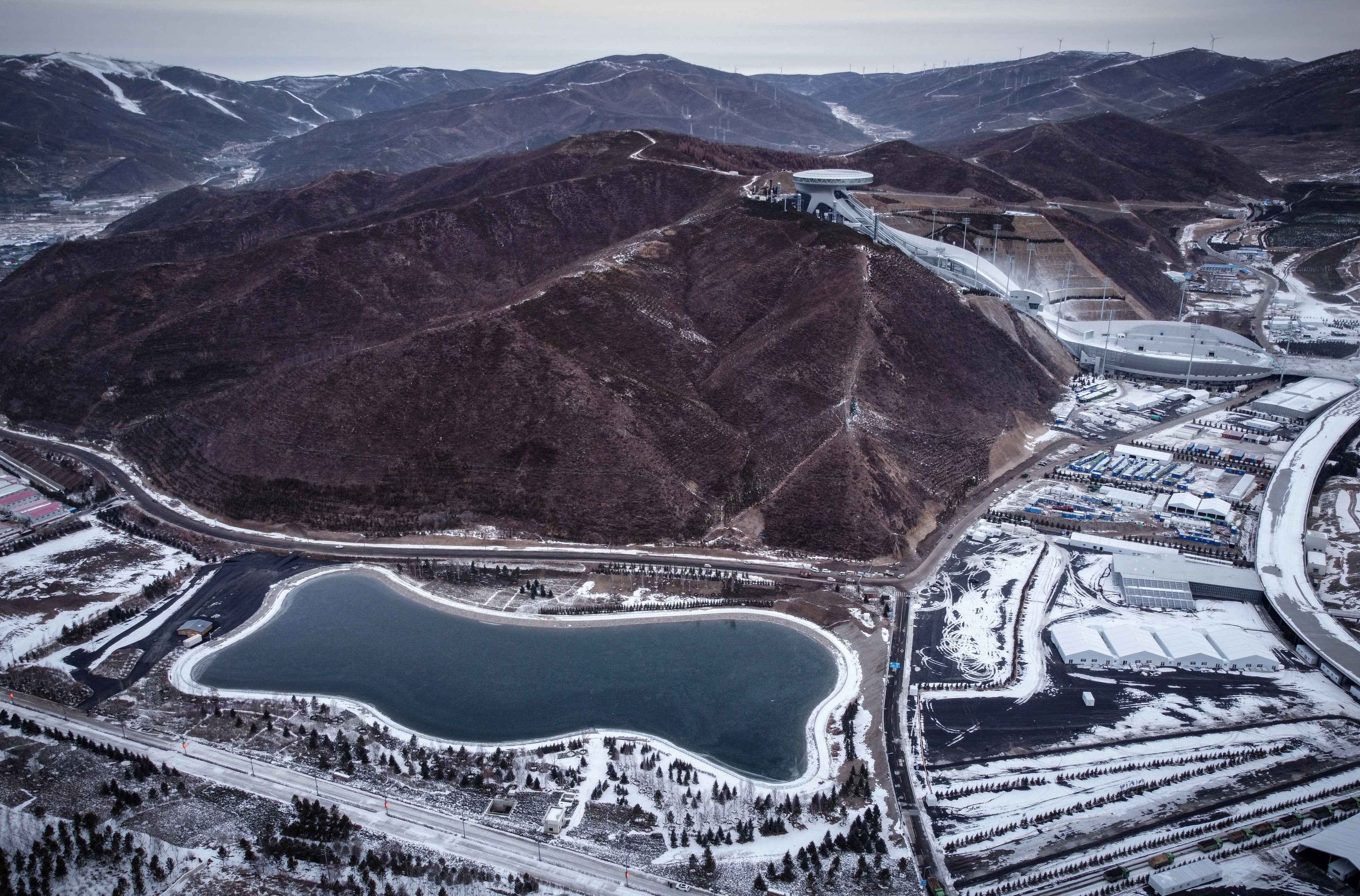 An aerial view shows a reservoir that provides water for snow guns that service competition venues of the Beijing 2022 Winter Olympics in Zhangjiakou, Hebei province, China, November 20, 2021. Pictured in the background is the National Ski Jumping Centre. Picture taken with a drone. REUTERS/Thomas Suen