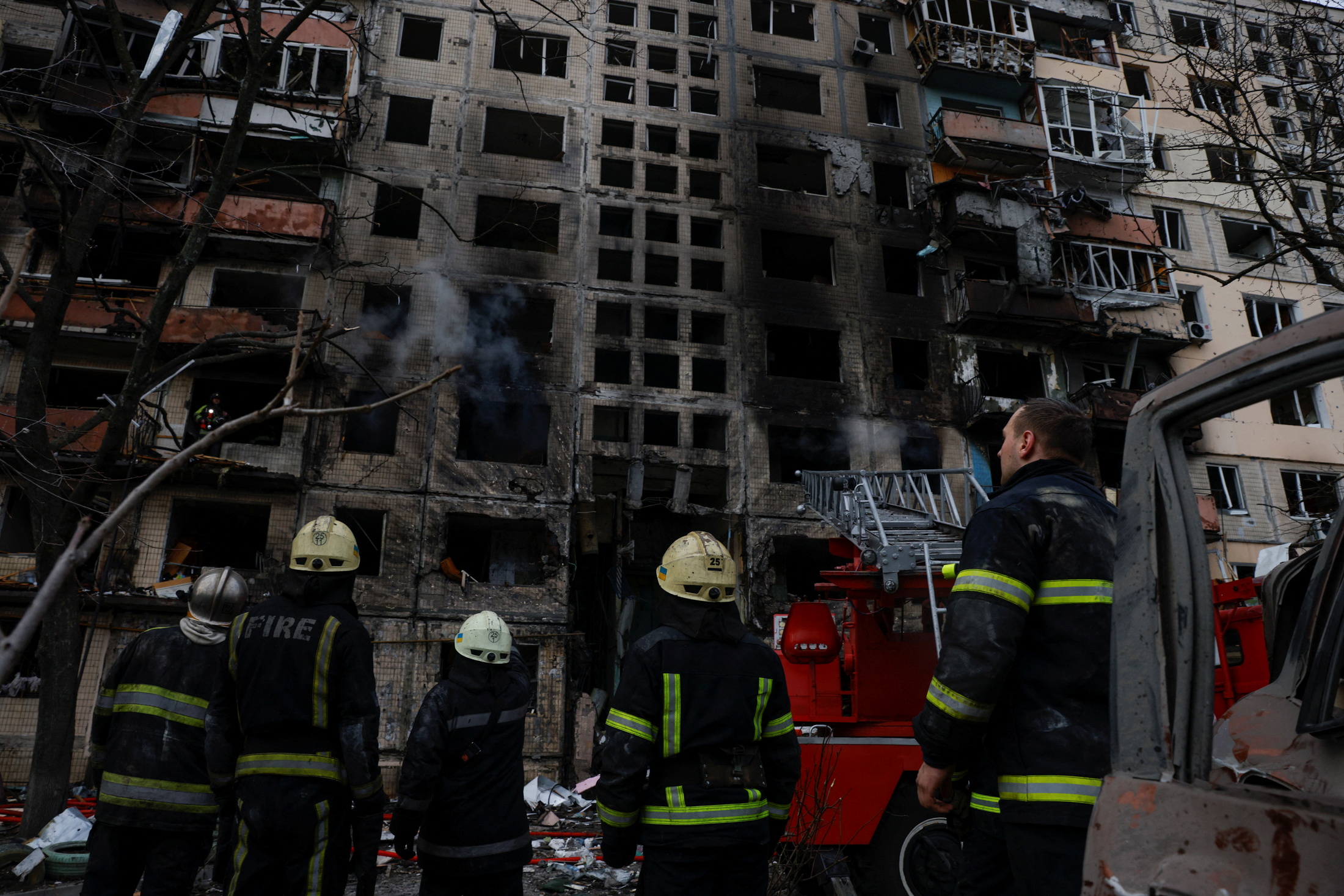Firefighters look at a residential building that was hit by a shell in the Obolon district in Kyiv