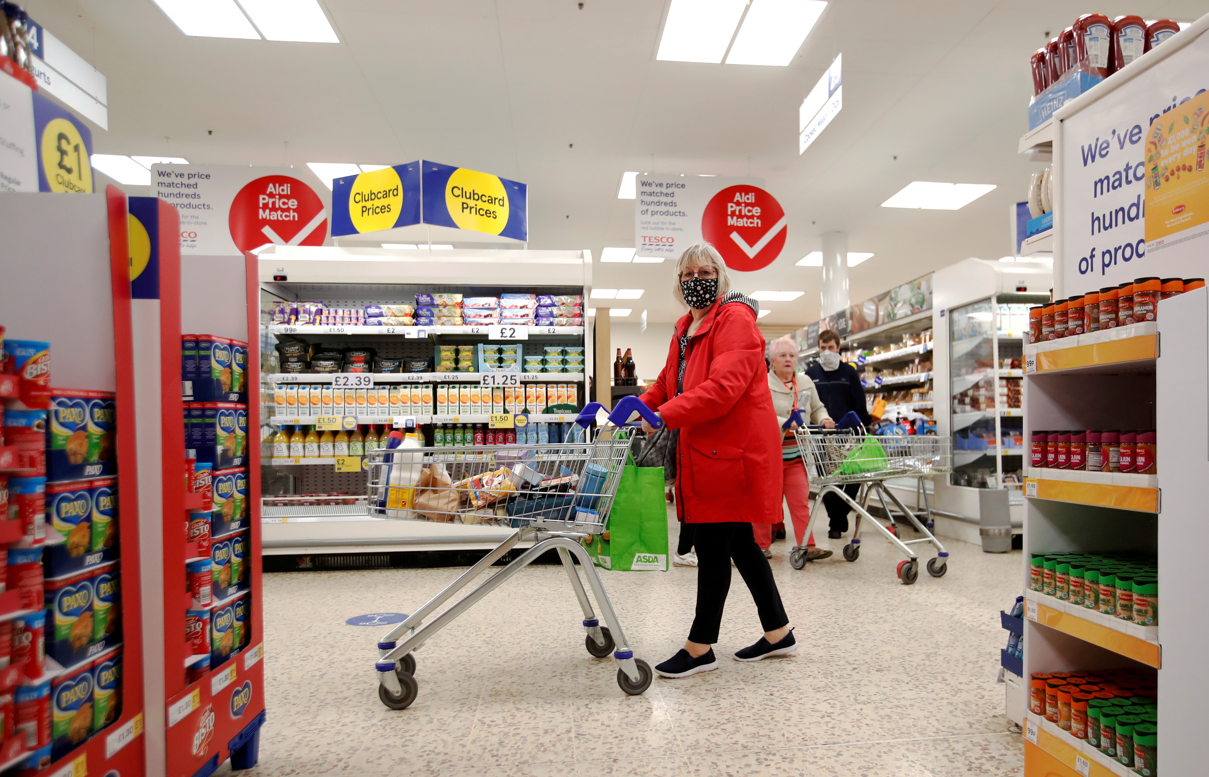 A woman wearing a face mask pushes a shopping cart at a Tesco supermarket in Hatfield, Britain