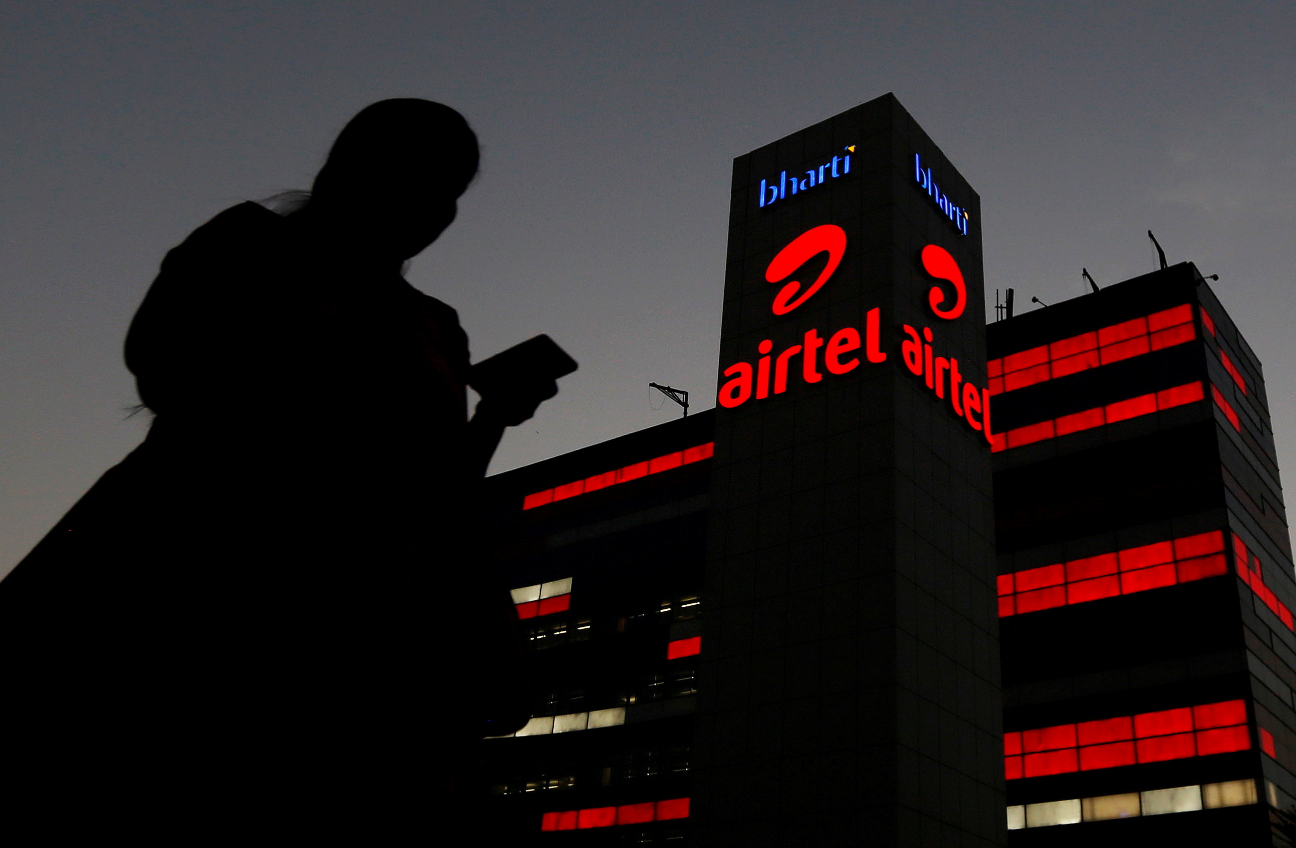 A girl checks her mobile phone as she walks past the Bharti Airtel office building in Gurugram