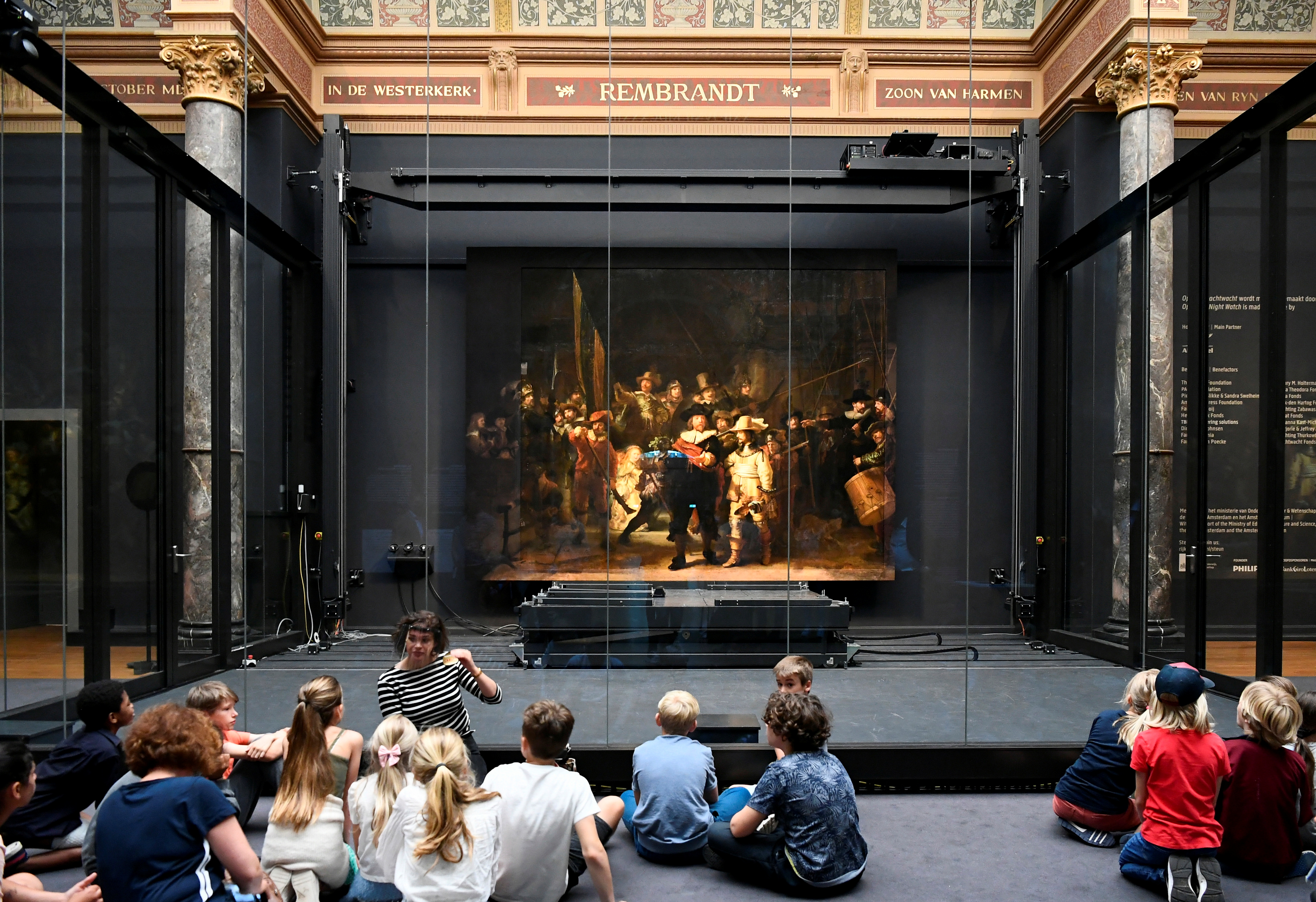 Children look at Rembrandt's famed Night Watch, which is back on display in what researchers say in its original size, with missing parts temporarily restored in an exhibition aided by artificial intelligence, at Rijksmuseum in Amsterdam, Netherlands June 23, 2021. REUTERS/Piroschka van de Wouw