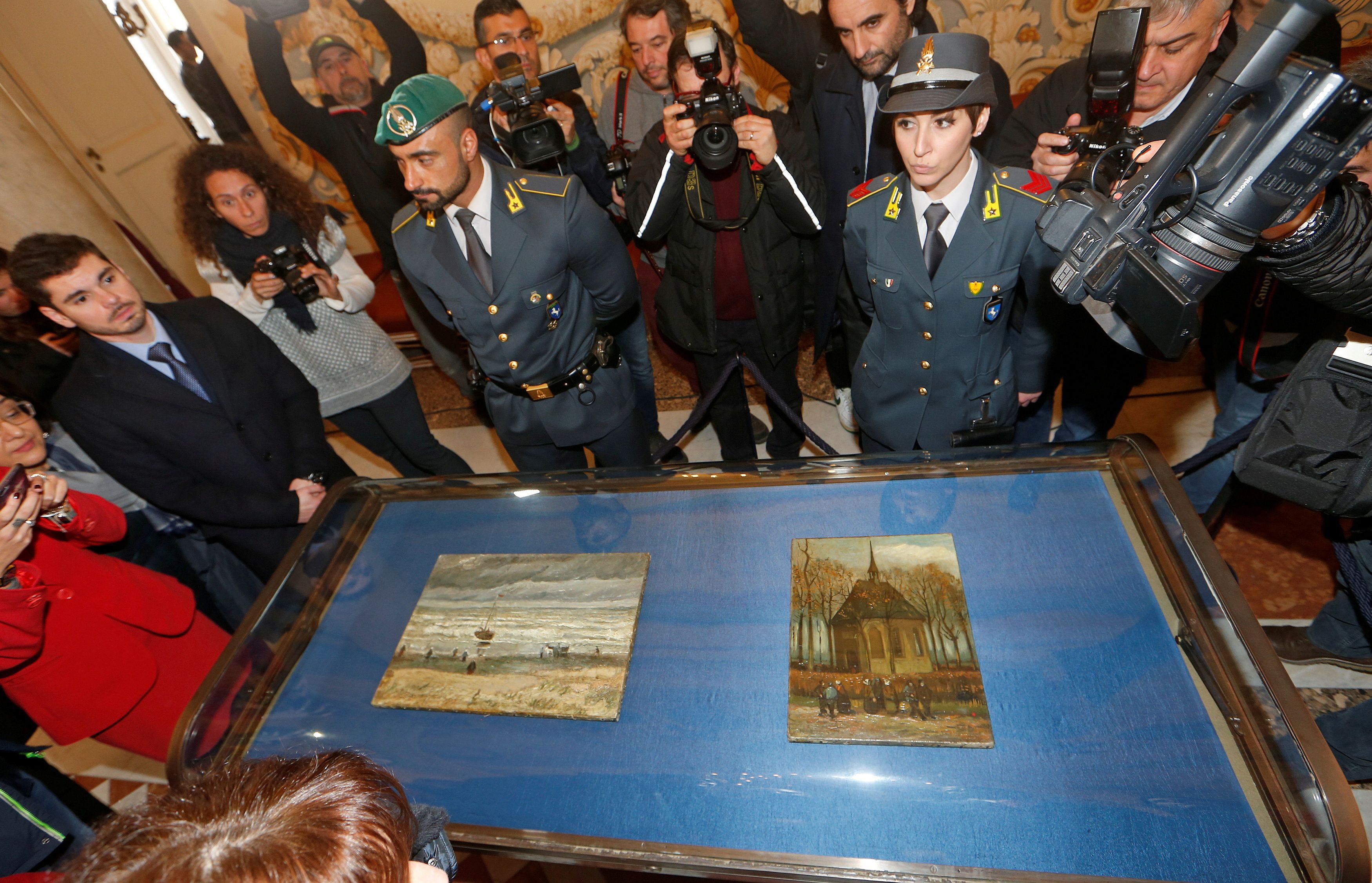People stand around a case containing two stolen Vincent Van Gogh paintings during a news conference in Capodimonte