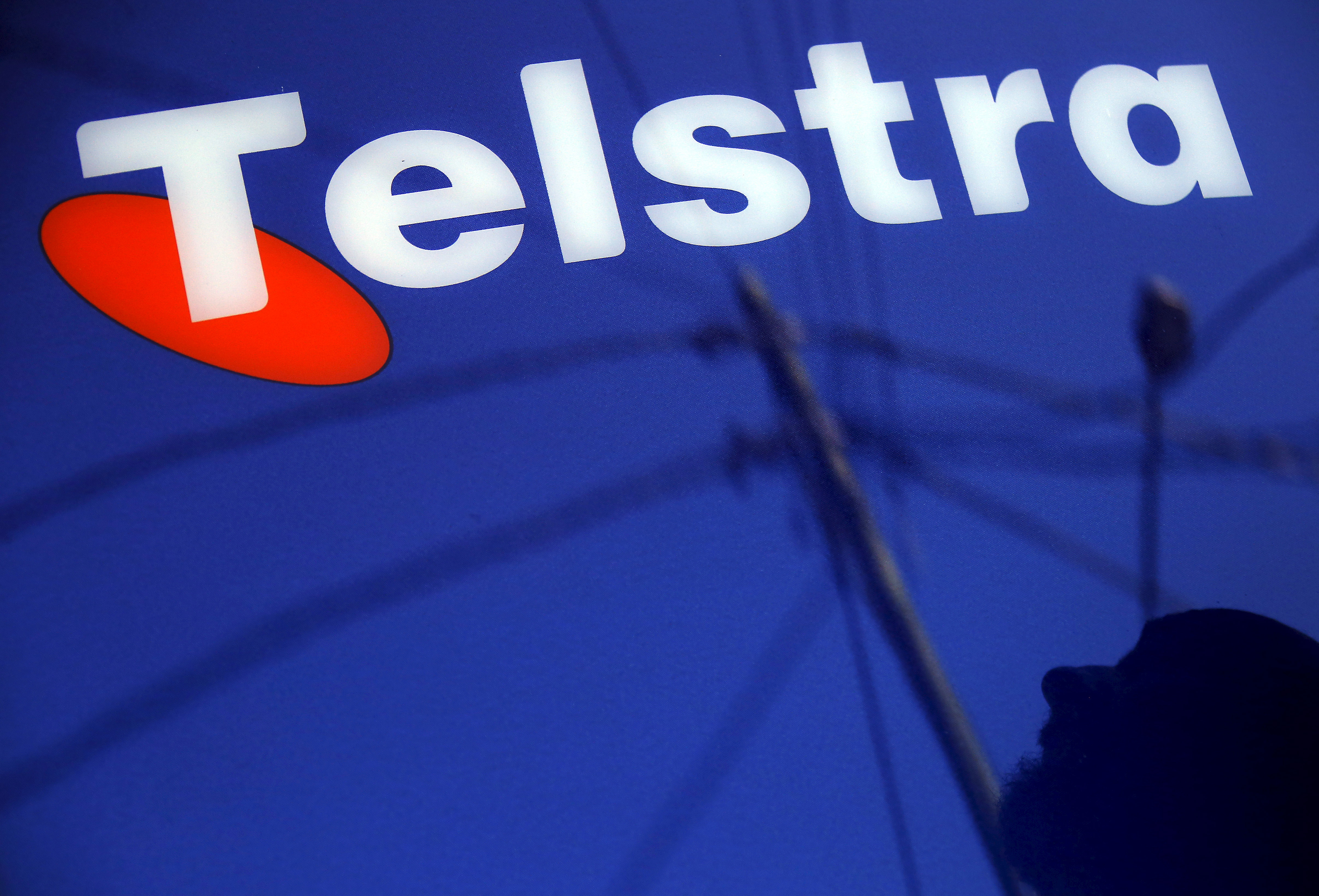 A man and power lines are reflected in a Telstra poster adorning a public telephone in Sydney, Australia