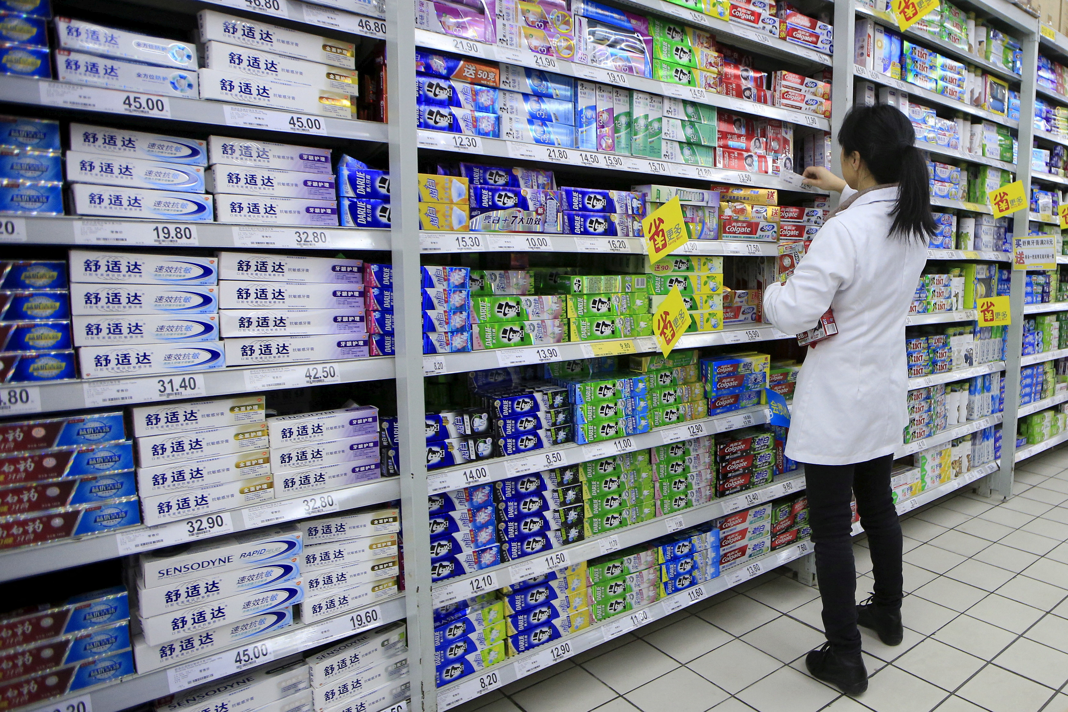 A salesperson arranges toothpaste products on a shelf at a supermarket in Shanghai