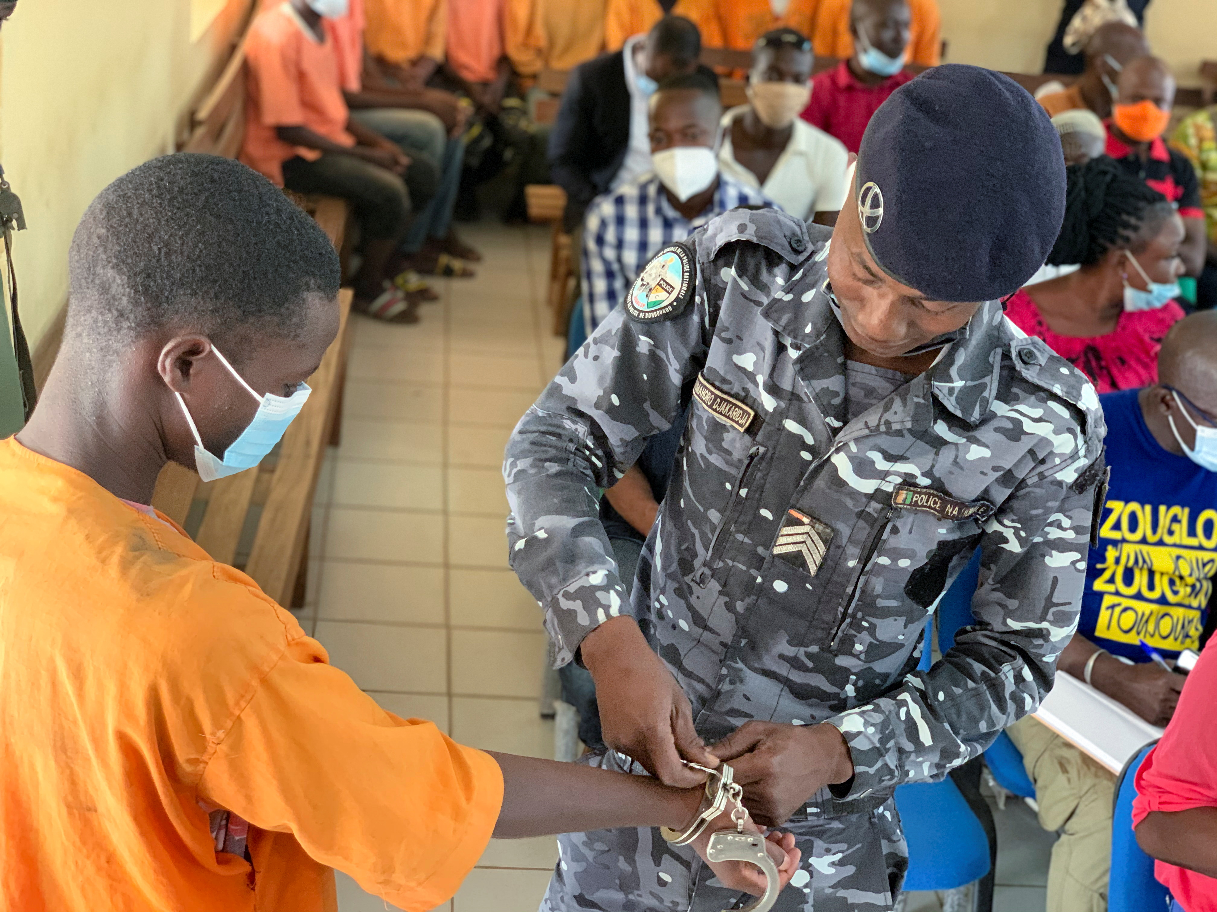 A police officer removes handcuffs from a man accused of child trafficking at a court in Bouna