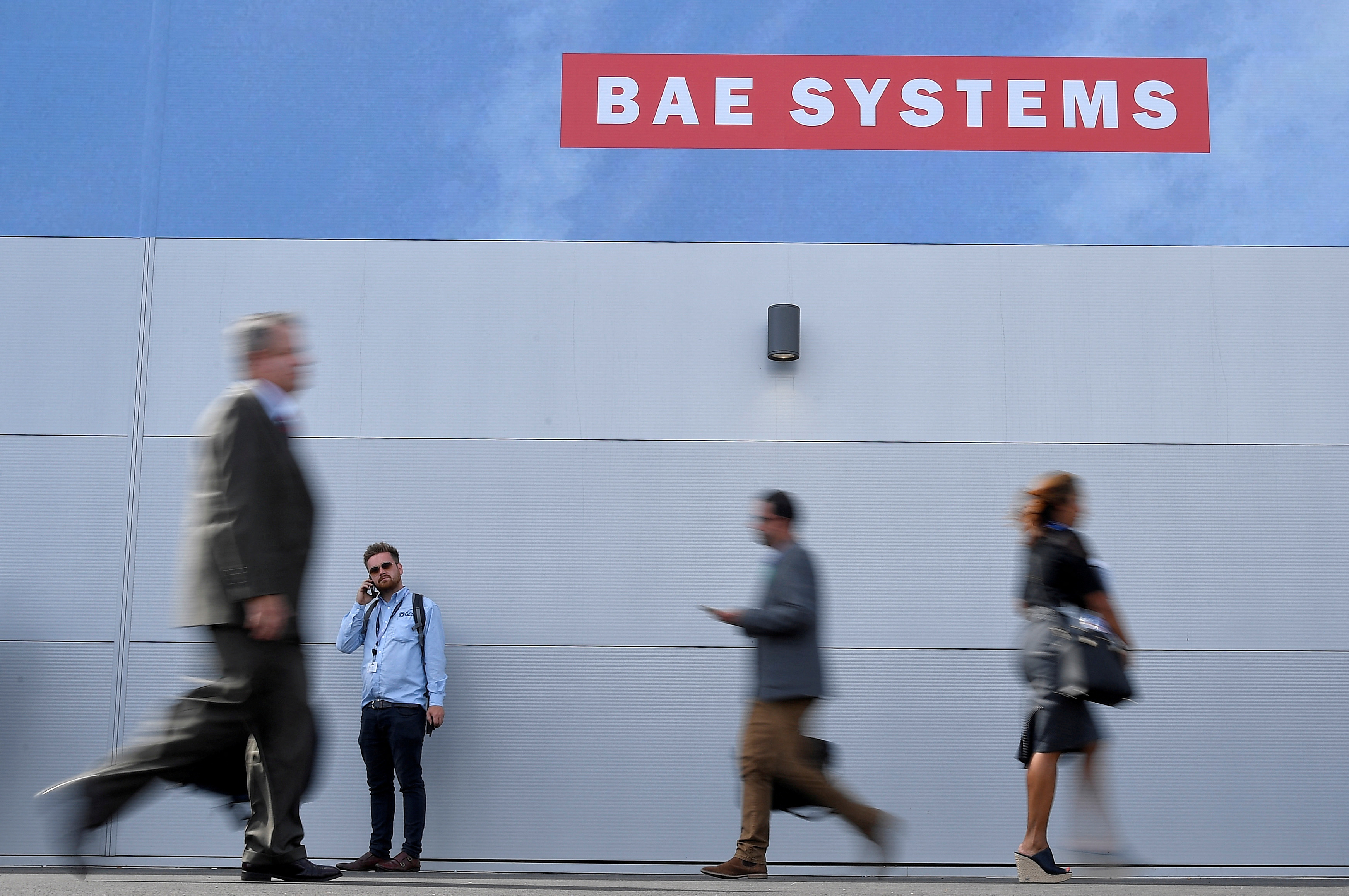 Trade visitors walk past an advertisement for BAE Systems at Farnborough International Airshow in Farnborough, Britain