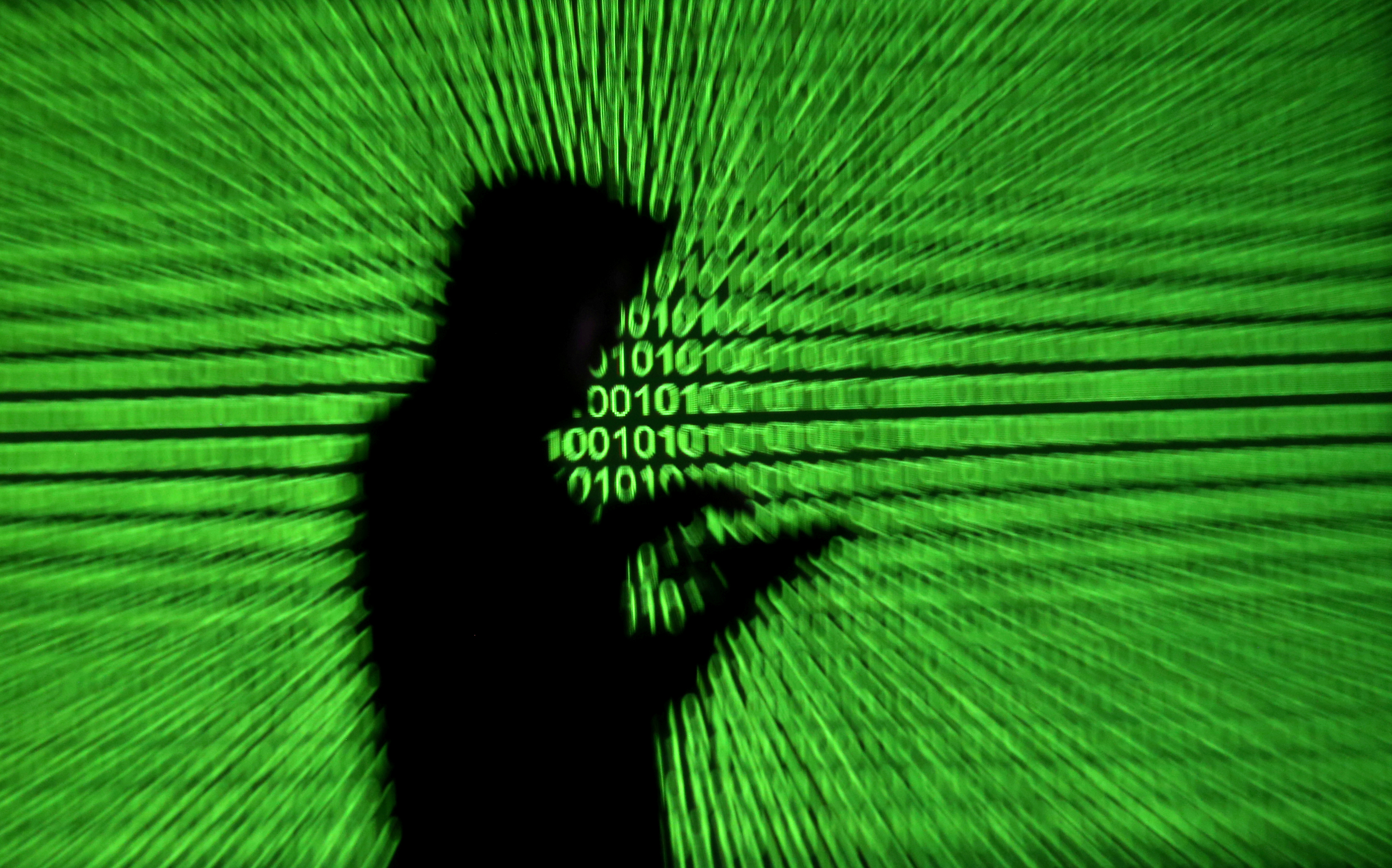 Silhouette of mobile device user is seen next to a screen projection of binary code are seen in this picture illustration