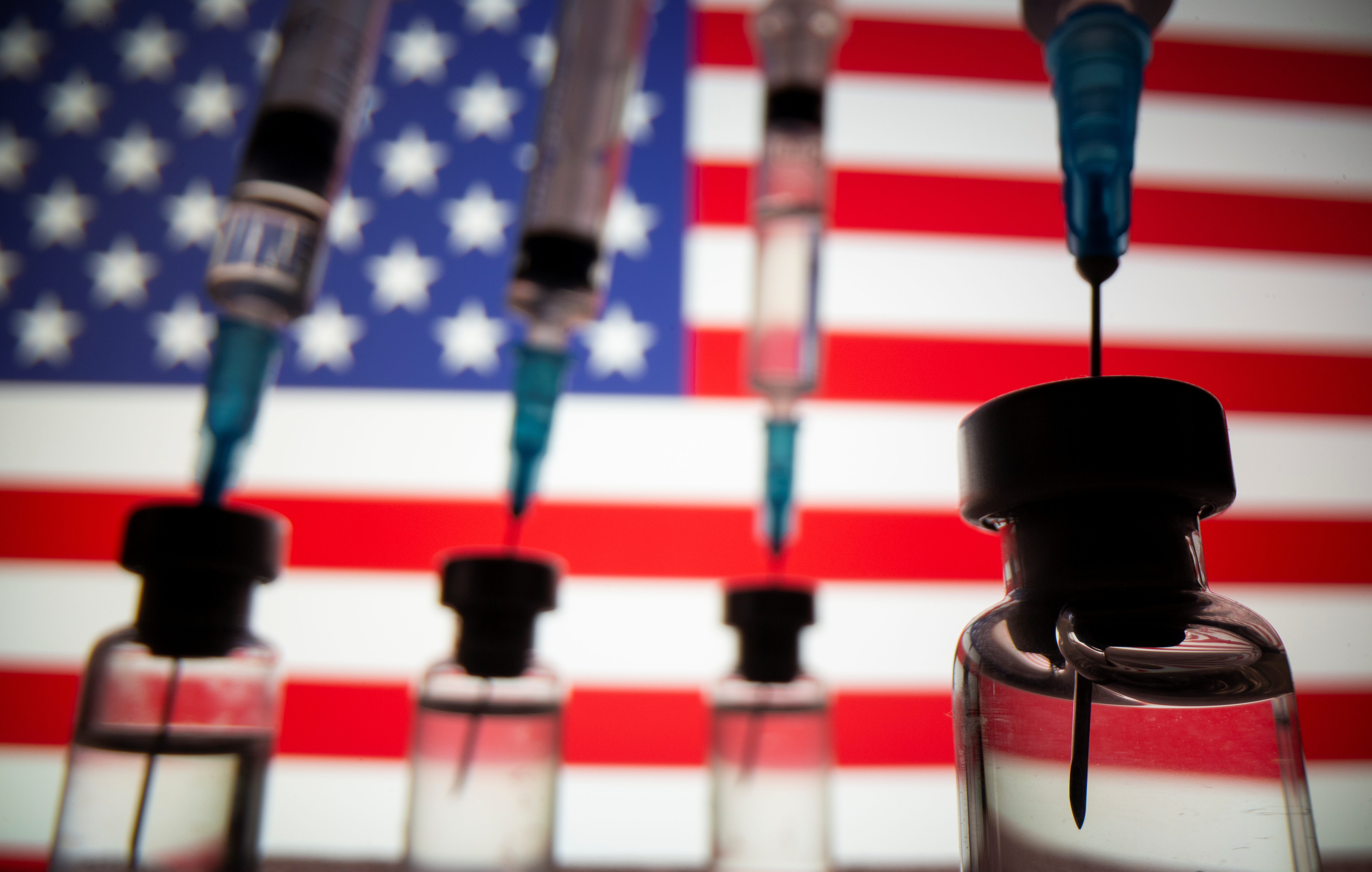 Vials and syringes are seen in front of displayed U.S. flag in this illustration photo