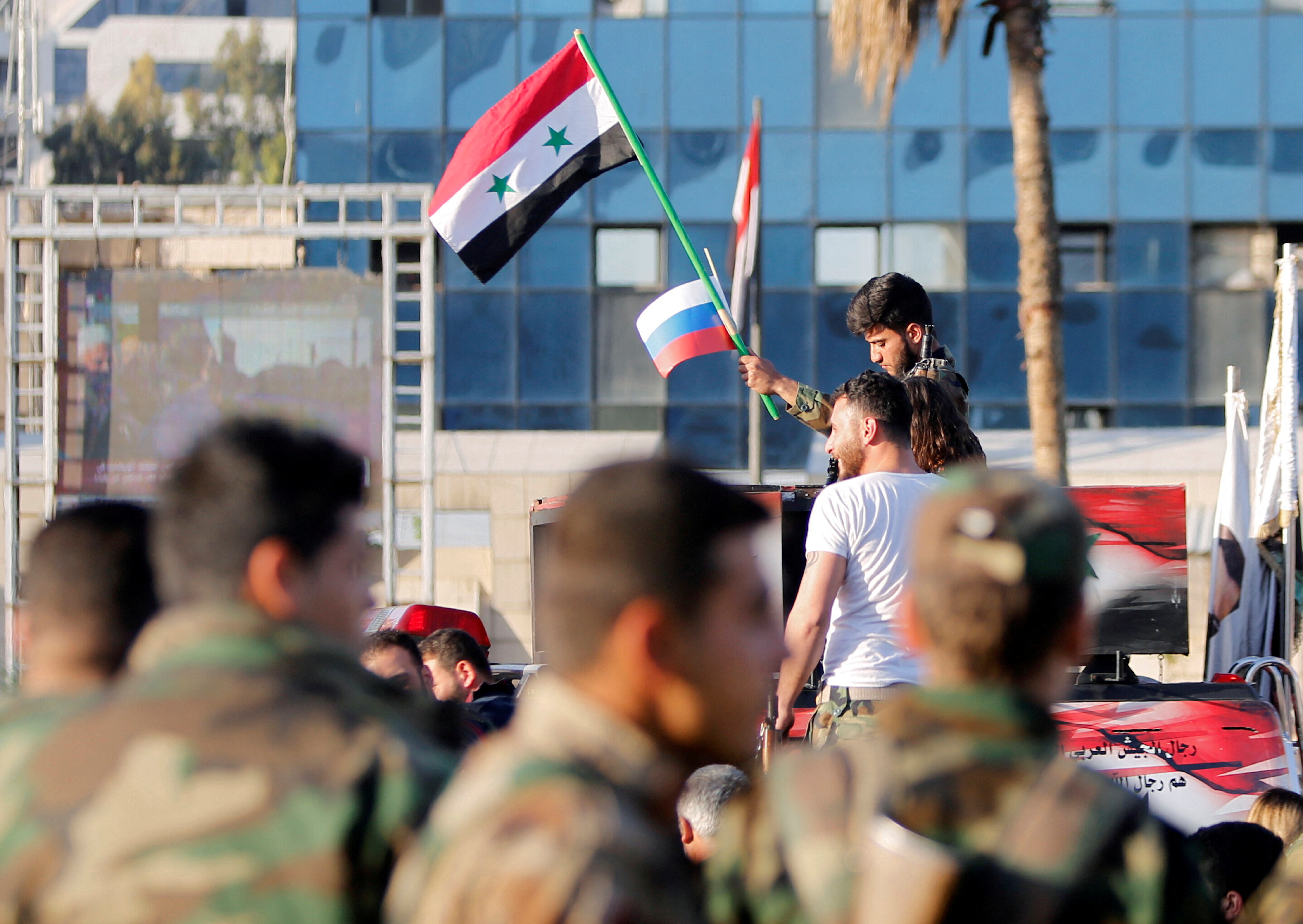 A Syrian soldier waves Russian and Syrian flags during a protest against air strikes in Damascus