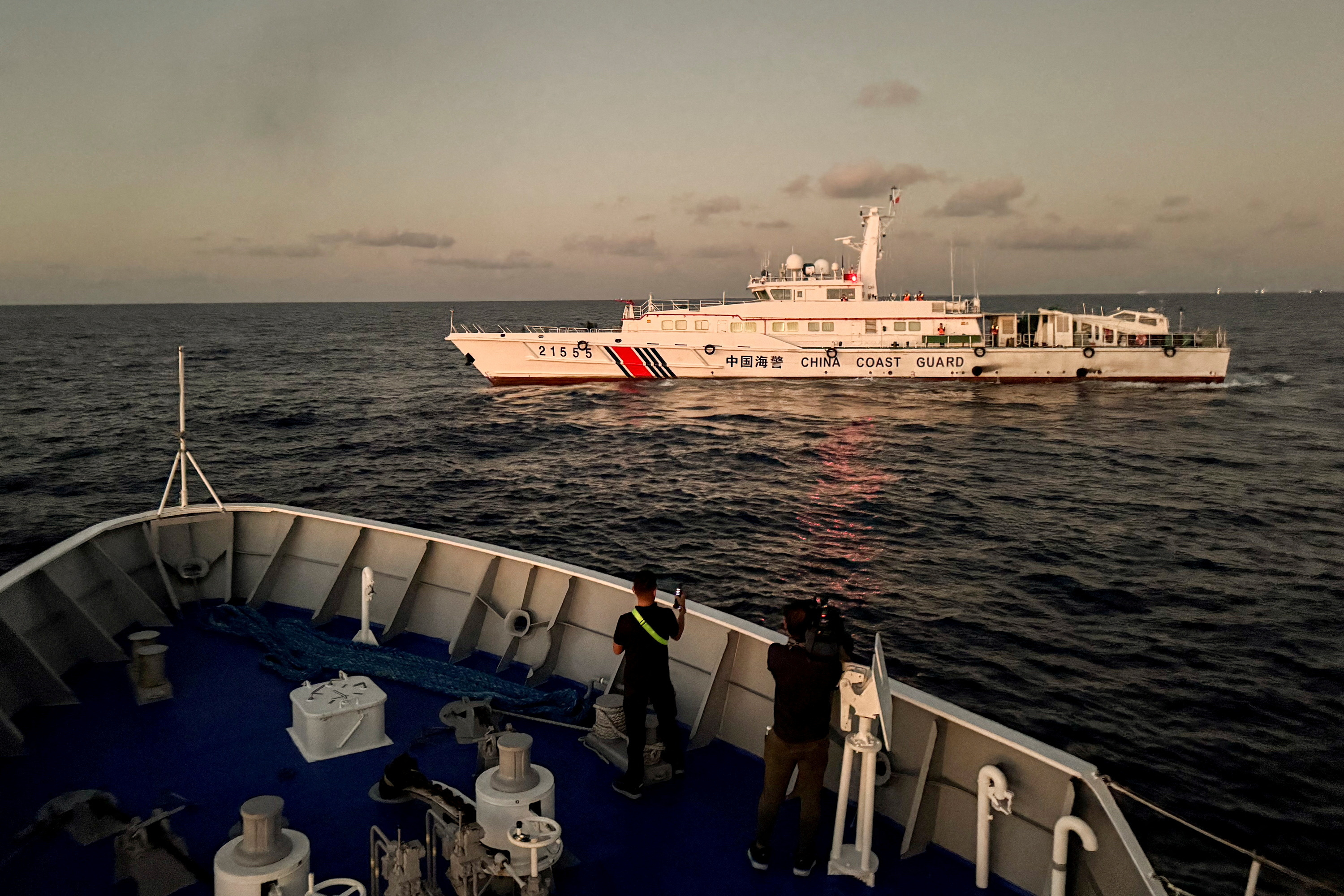 Members of the media take footage of a Chinese Coast Guard vessel blocking a Philippine Coast Guard vessel on its way to a resupply mission at Second Thomas Shoal in the South China Sea