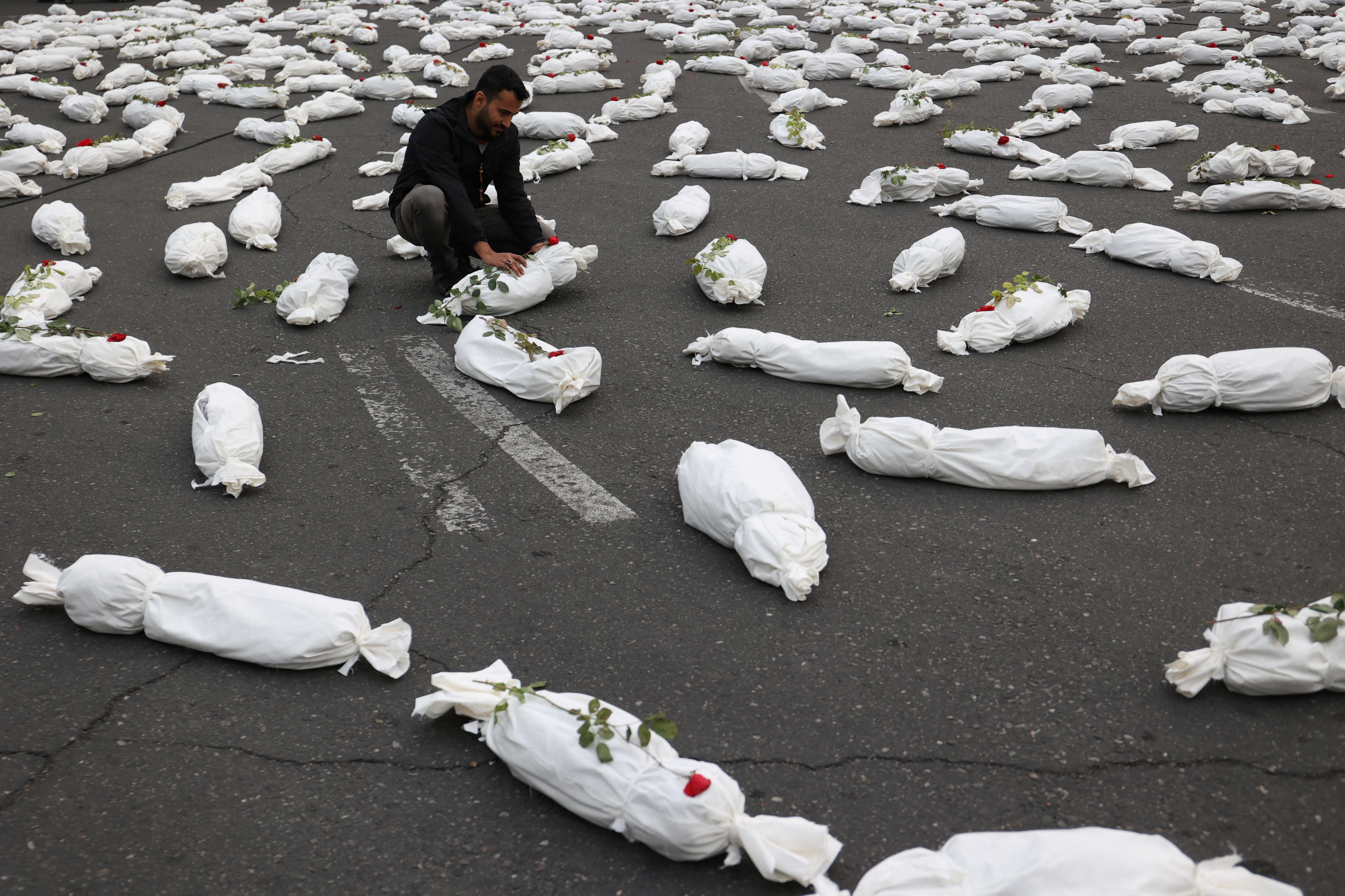 An Iranian man sits next to the symbolic shrouds of Gaza children's dead bodies during a gesture in a street in Tehran