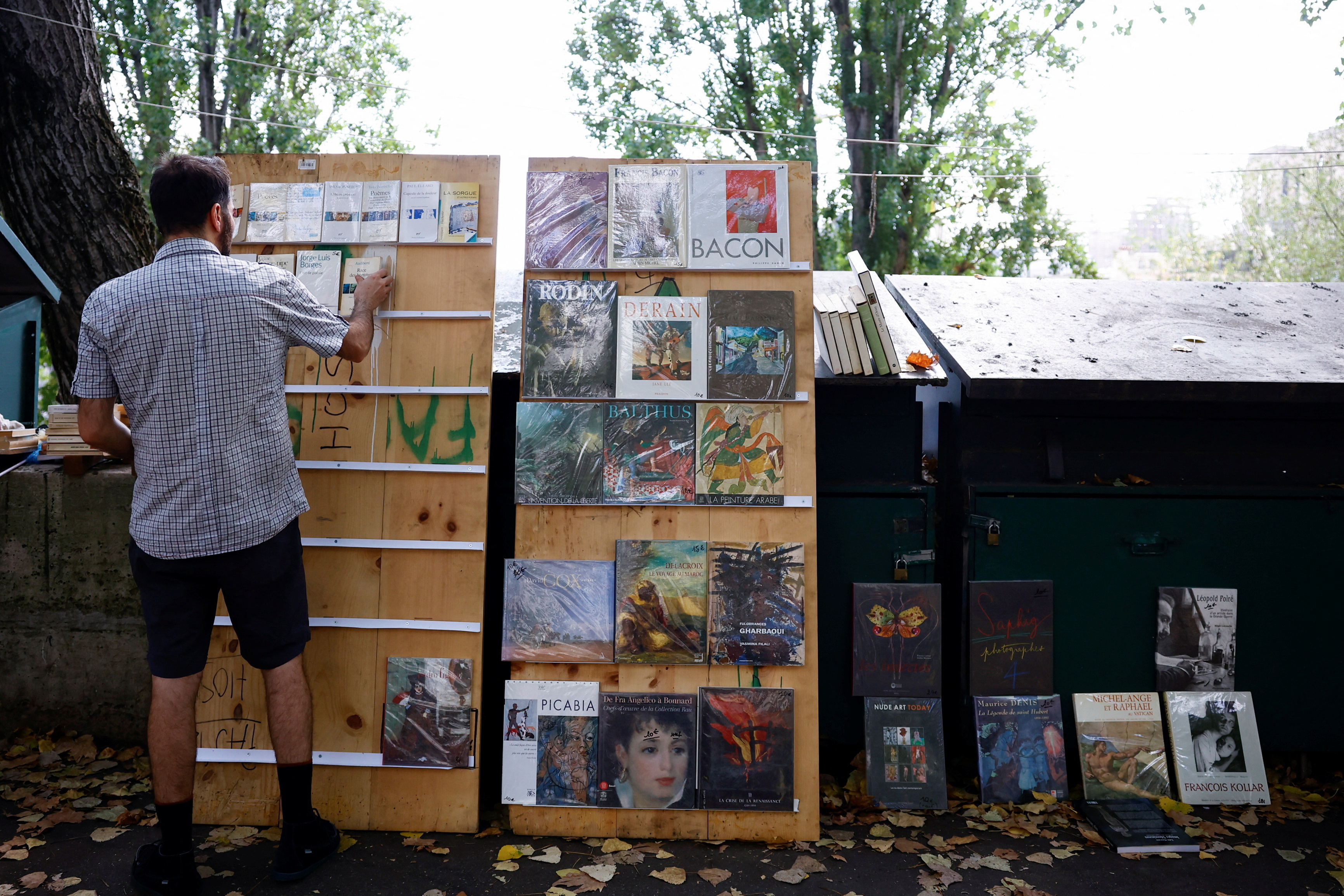 New Parisian bouquiniste, traditional street bookseller, places books on shelves along the banks of the River Seine in Paris