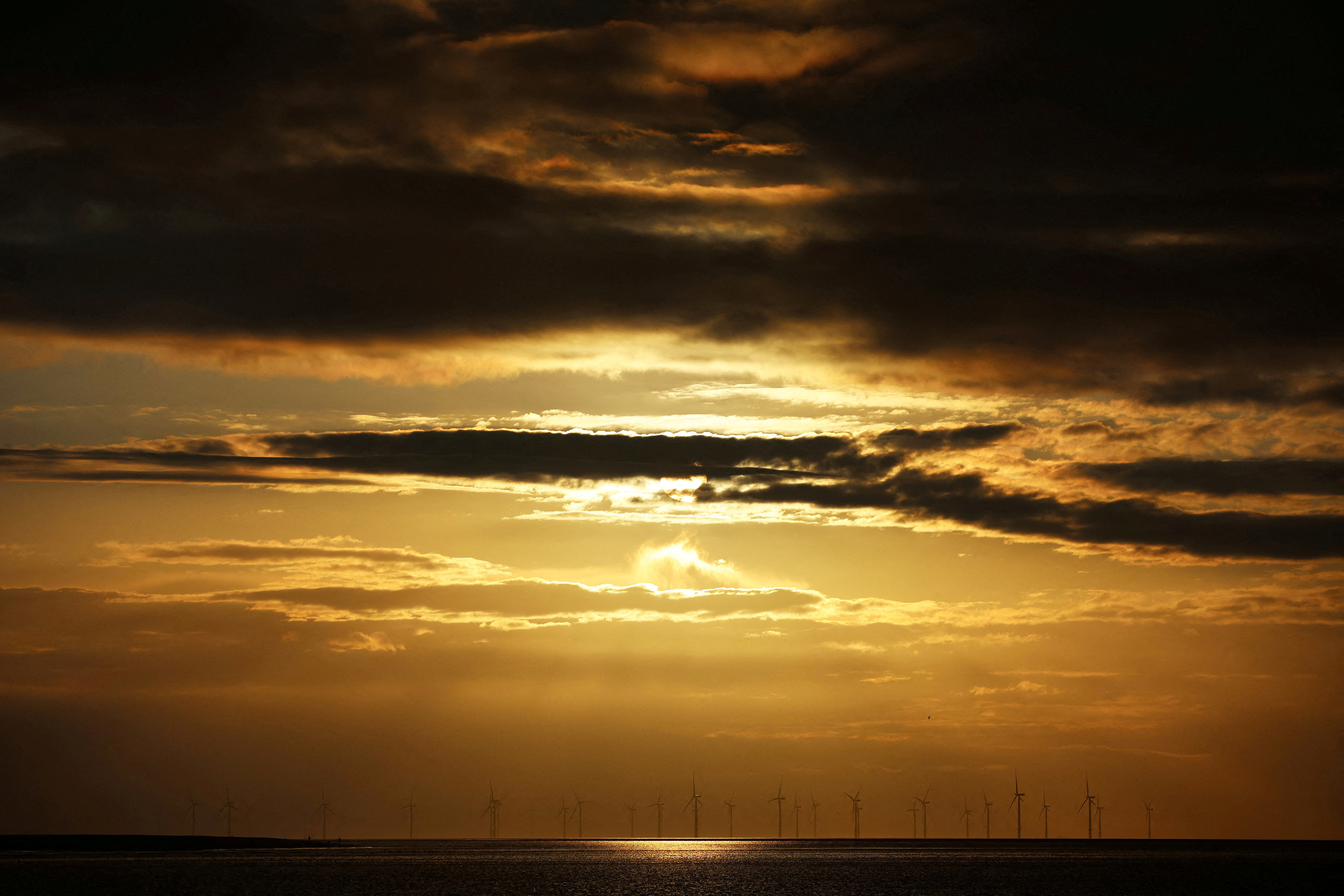The sun sets behind wind turbines on the Burbo Bank wind farm in the Mersey Estuary in Liverpool