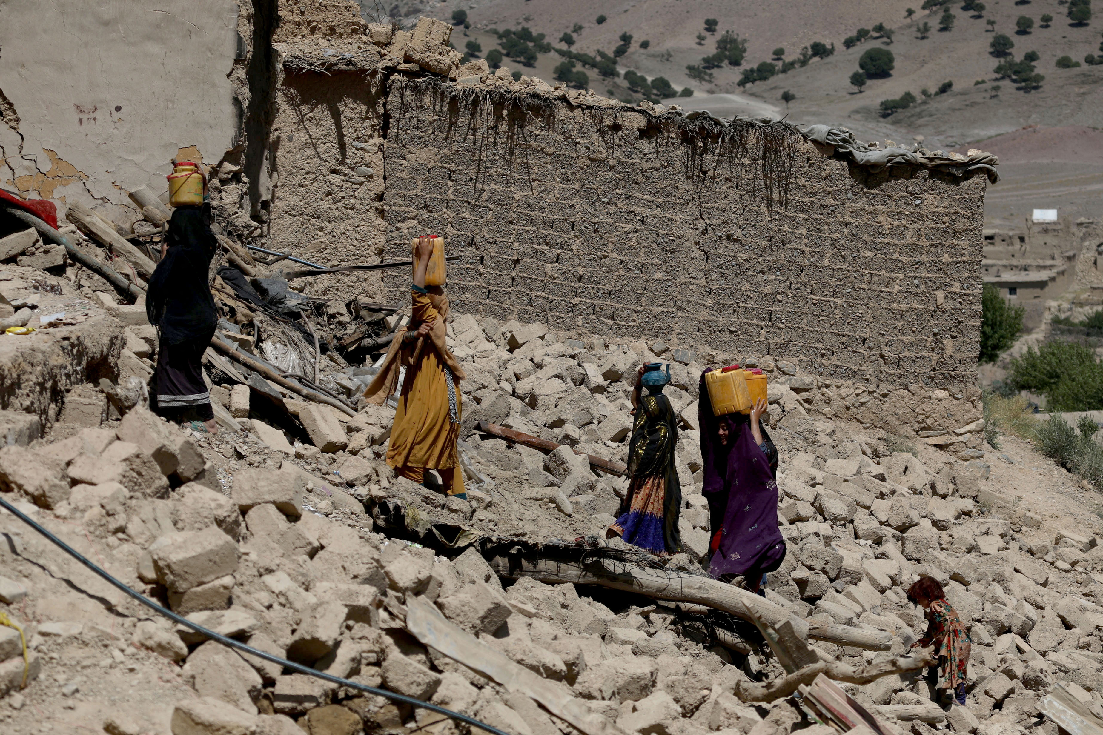 Afghan women carry water containers through the debris of damaged houses after the recent earthquake in Wor Kali village