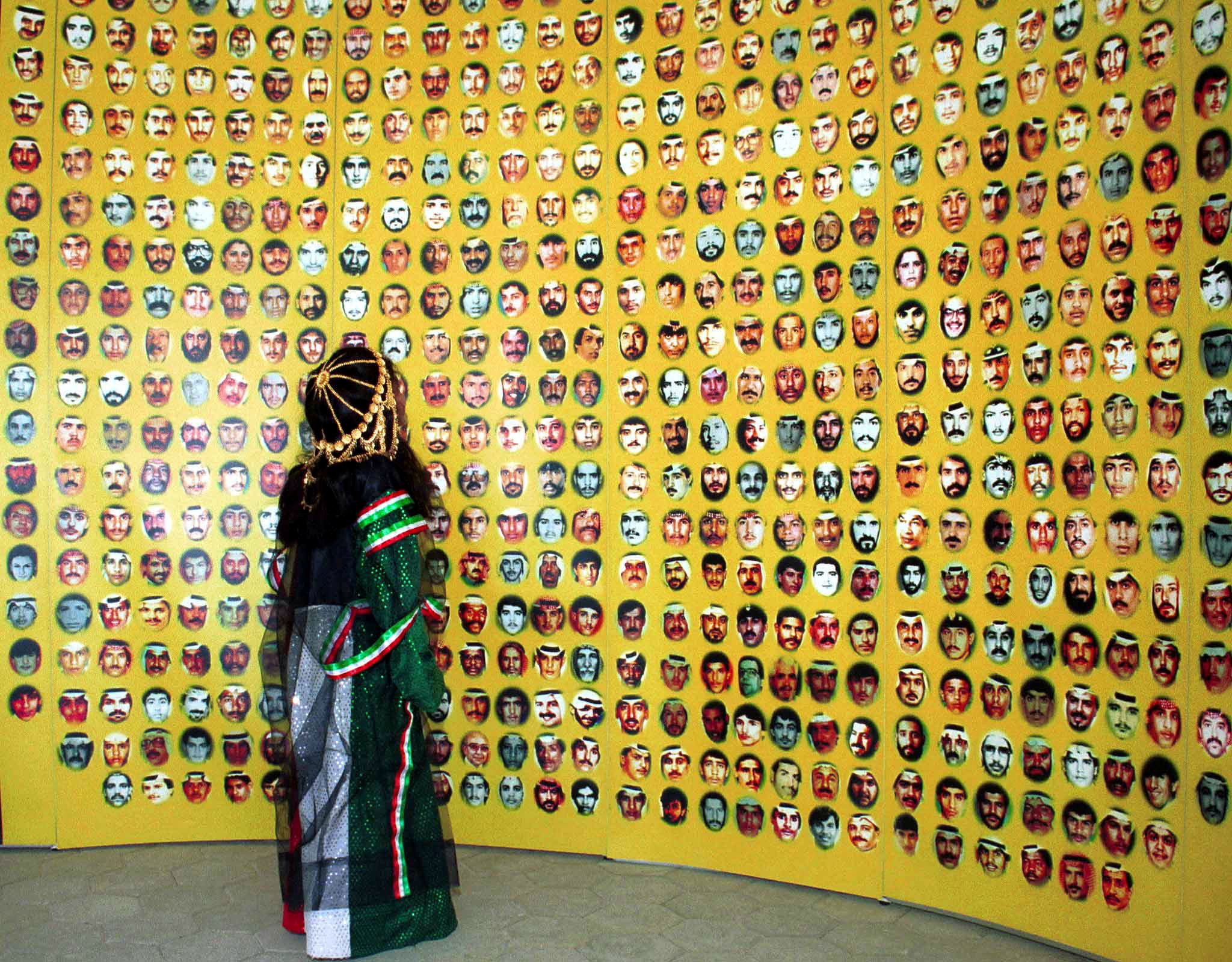 A young girl in Kuwaiti national dress looks up at pictures of hundreds of people missing since the ..