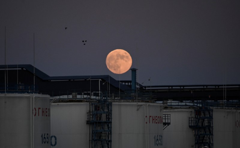 The moon rises behind oil storage tanks in Omsk