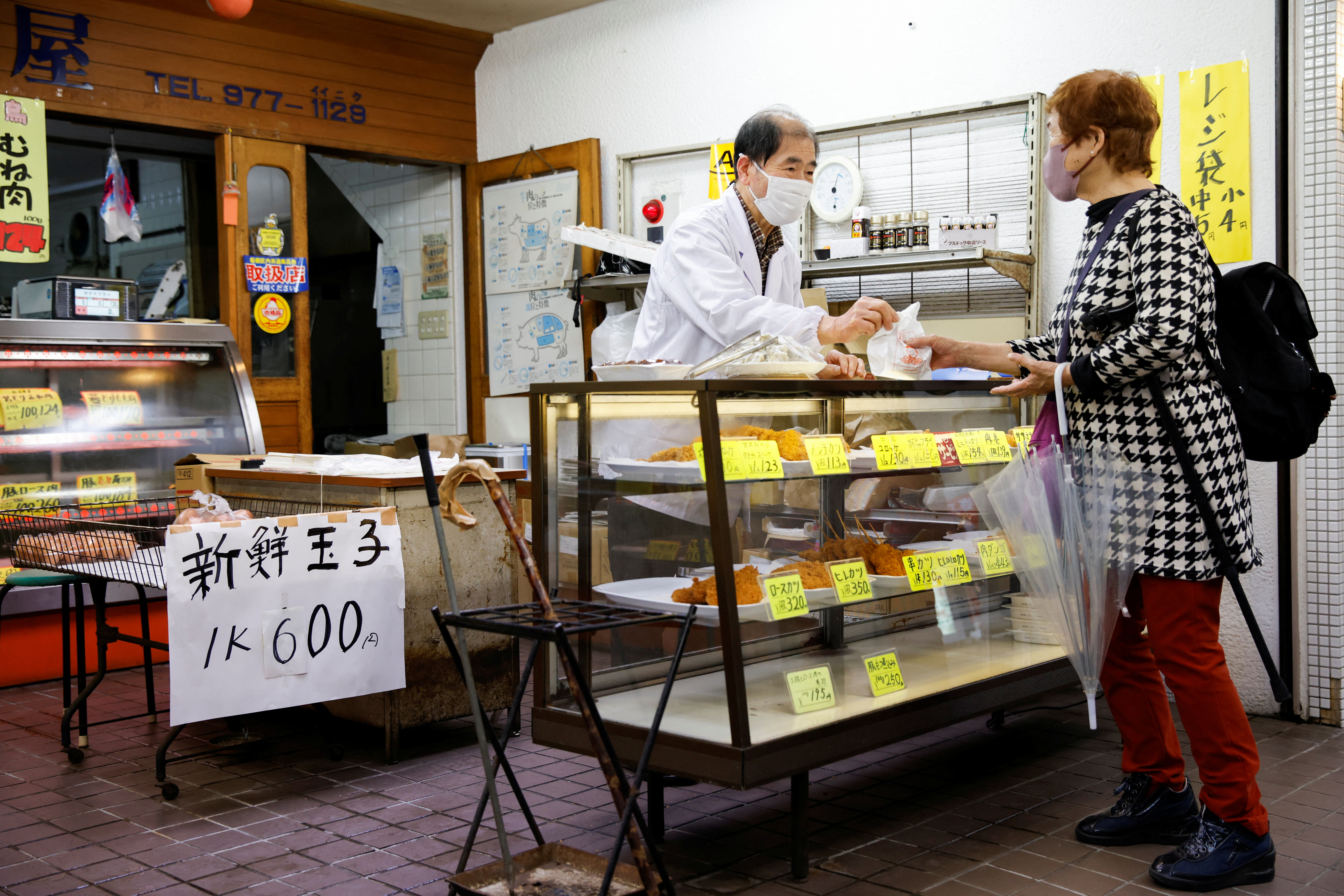 A customer buys food at a shop selling cooked food at a market in Tokyo