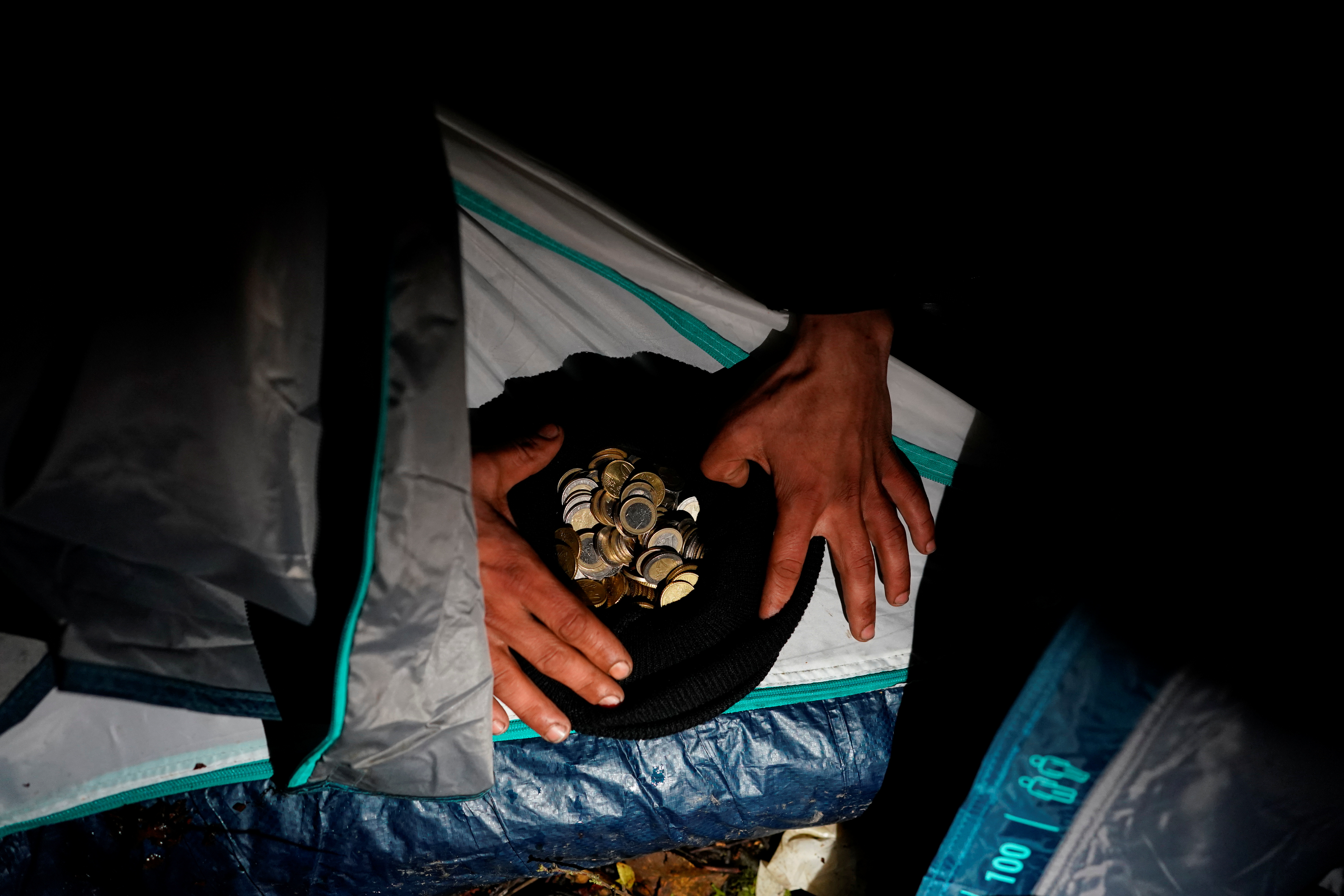 Kurdish Iraqi migrant Dawan Anwar Mahmud counts the coins he made selling sandwiches in his tent at a makeshift camp in Loon-Plage near Dunkirk, France, November 29, 2021. REUTERS/Juan Medina 