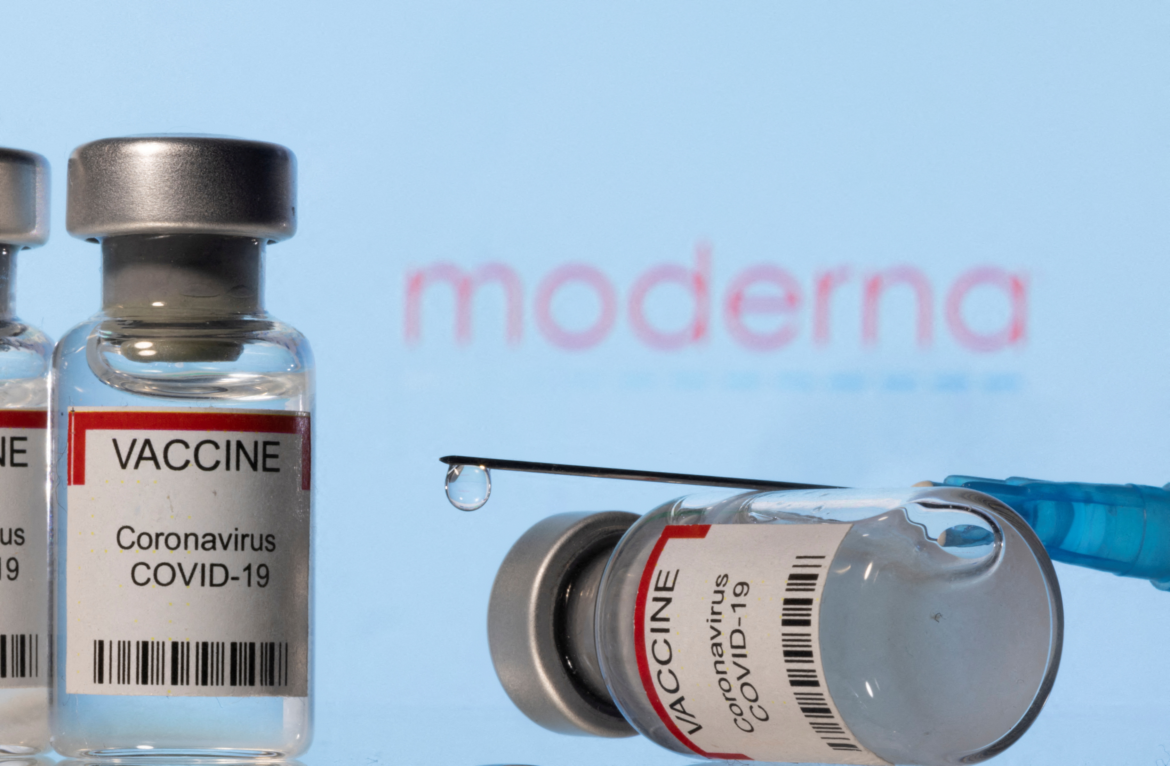 Illustration shows vials labelled "VACCINE Coronavirus COVID-19" and a syringe in front of a displayed Moderna logo