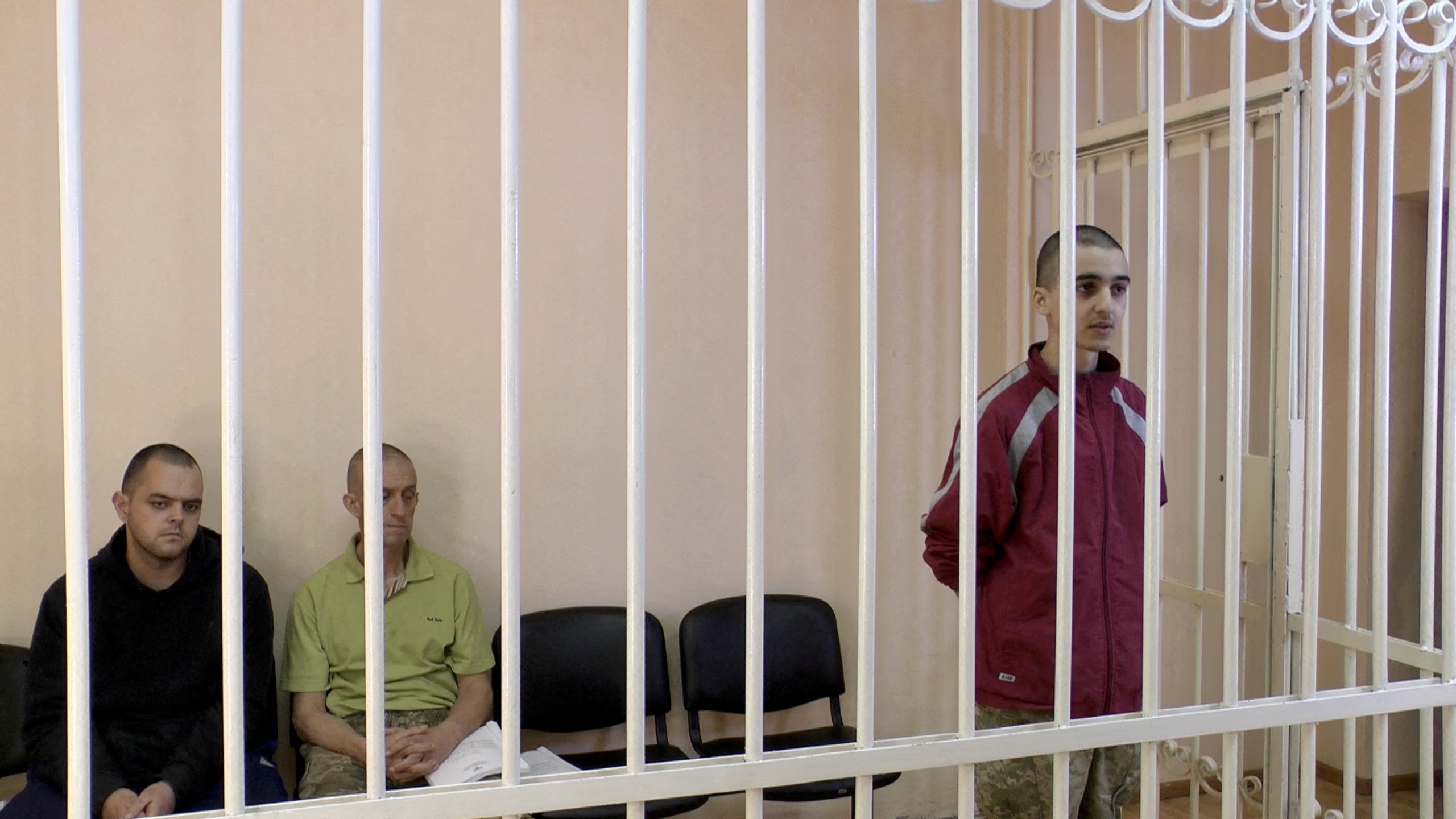 FILE PHOTO: A still image shows Britons Aiden Aslin, Shaun Pinner and Moroccan Brahim Saadoun in a courtroom cage at a location given as Donetsk