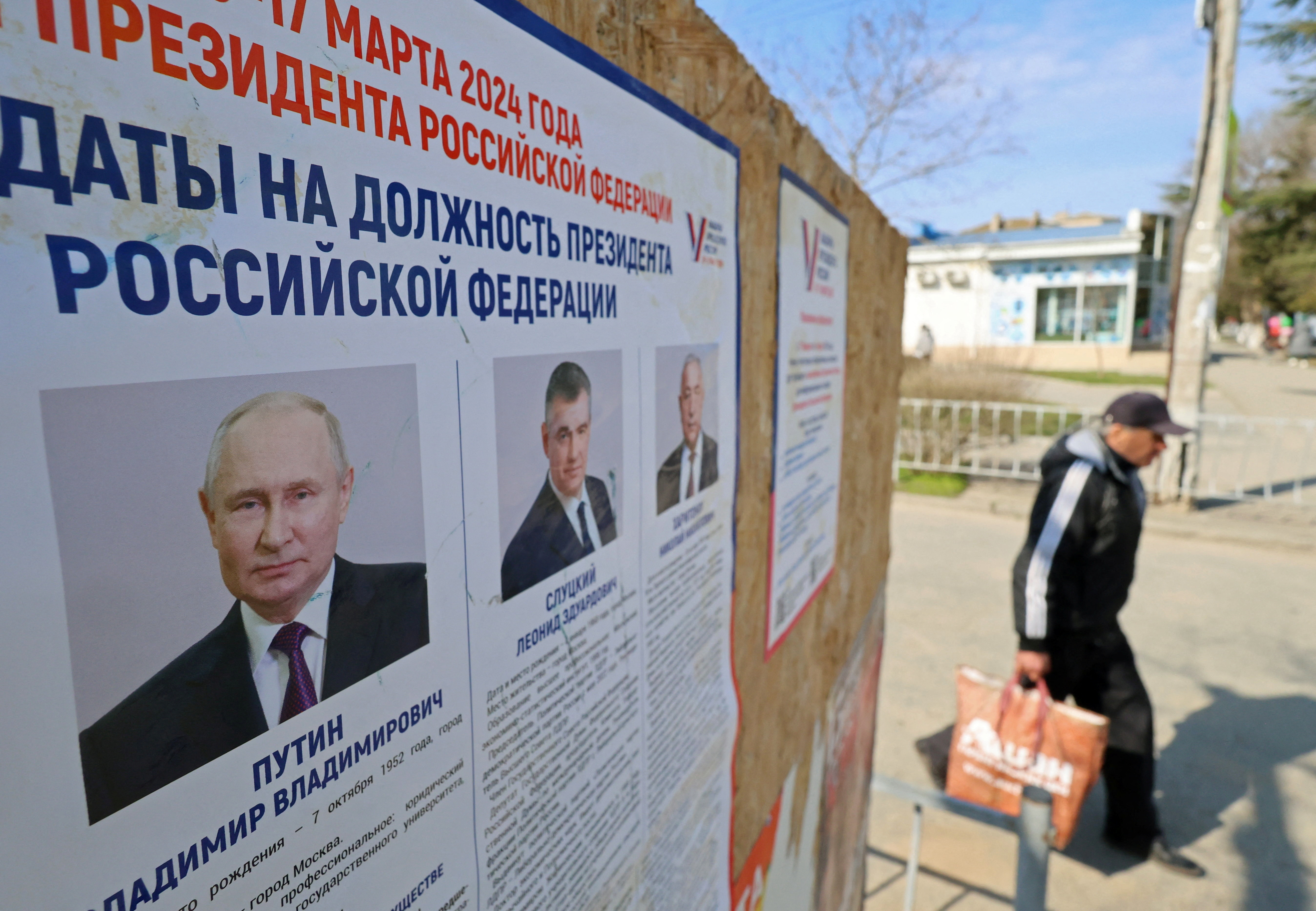 A man walks past an information board with portraits of Russian presidential candidates in the upcoming election in Yevpatoriya