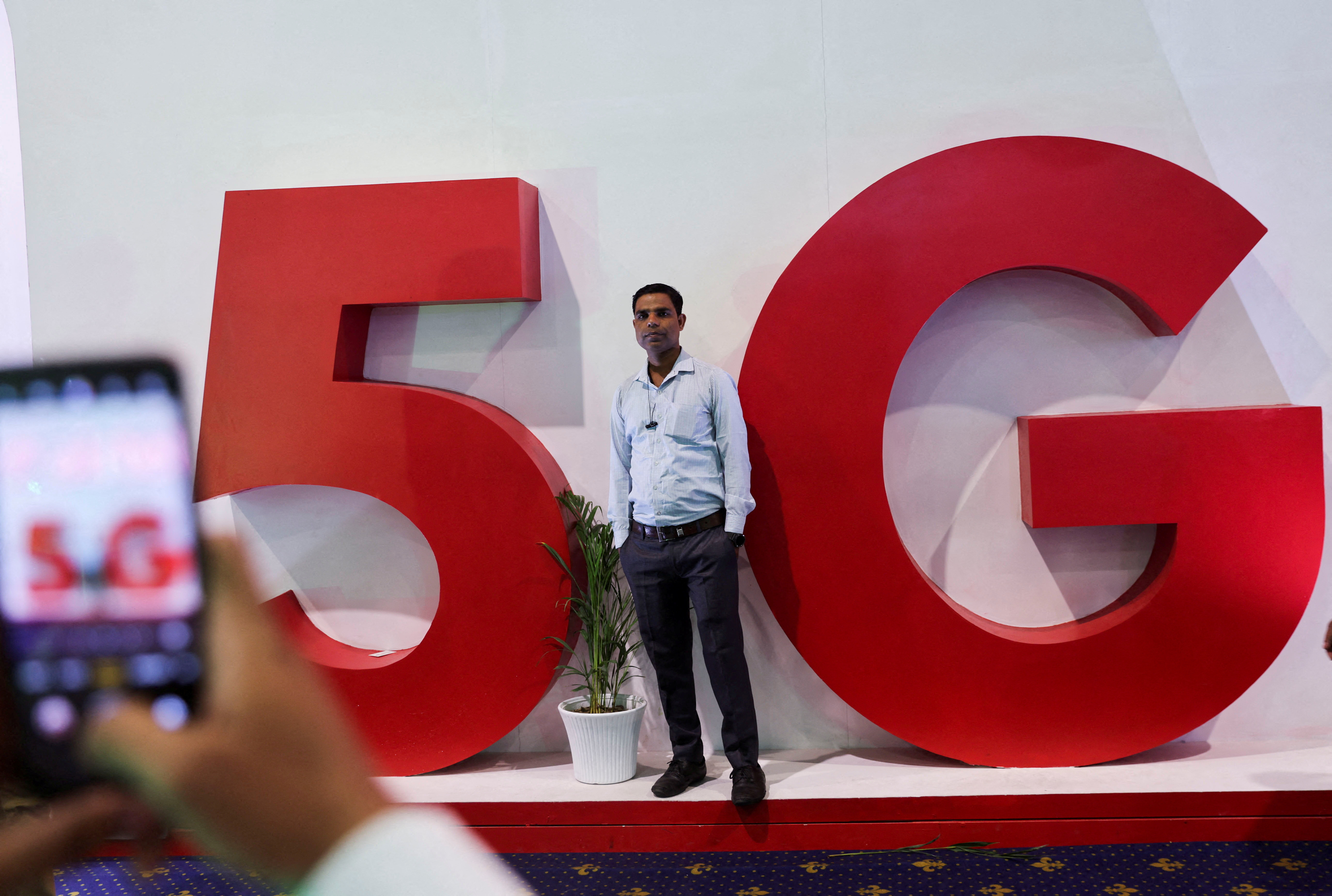 A man takes a picture of a friend in front of a sign showing installation of the 5G network