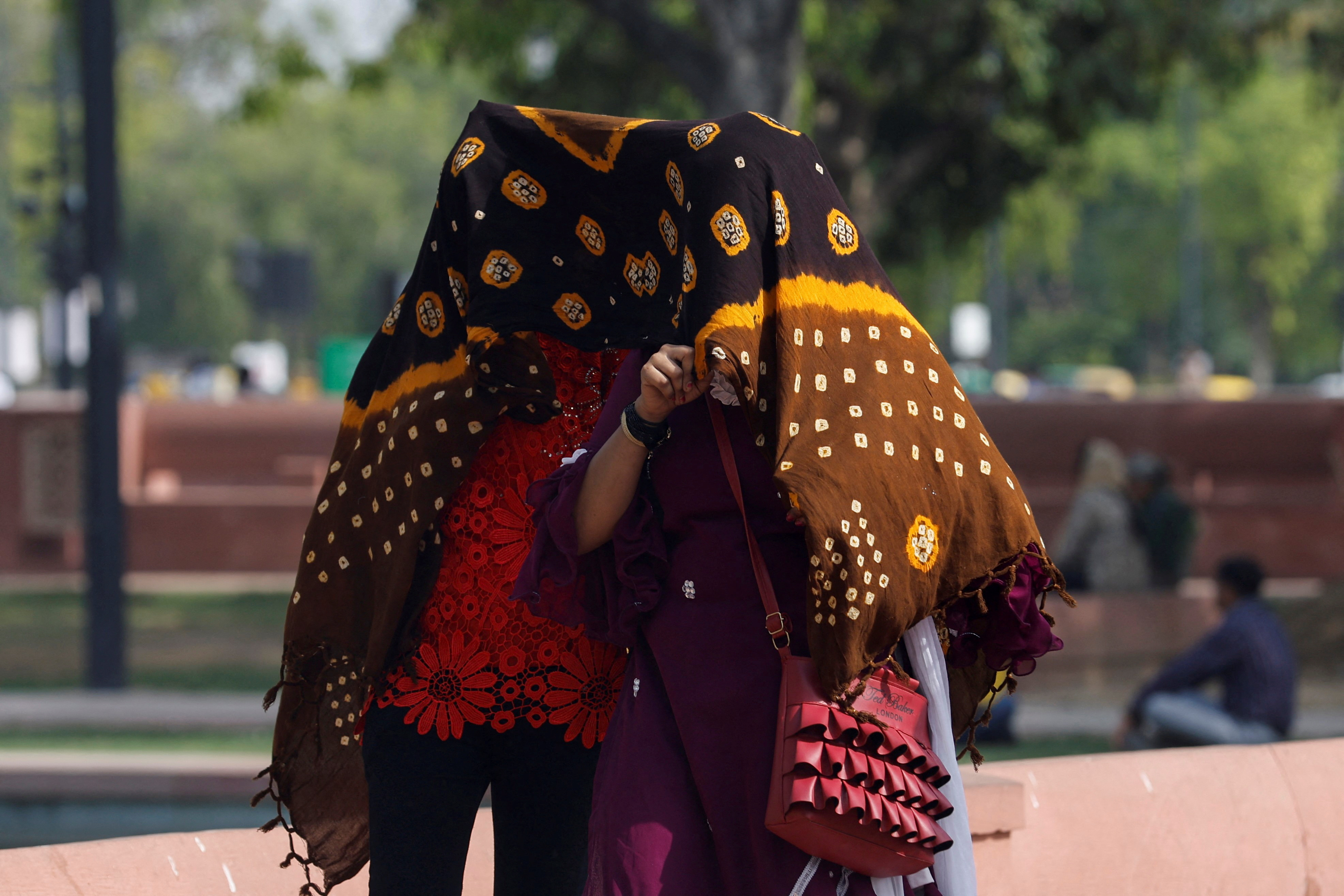 Women take shelter under a cloth, as they walk across a garden on a hot summer day near India Gate, in New Delhi
