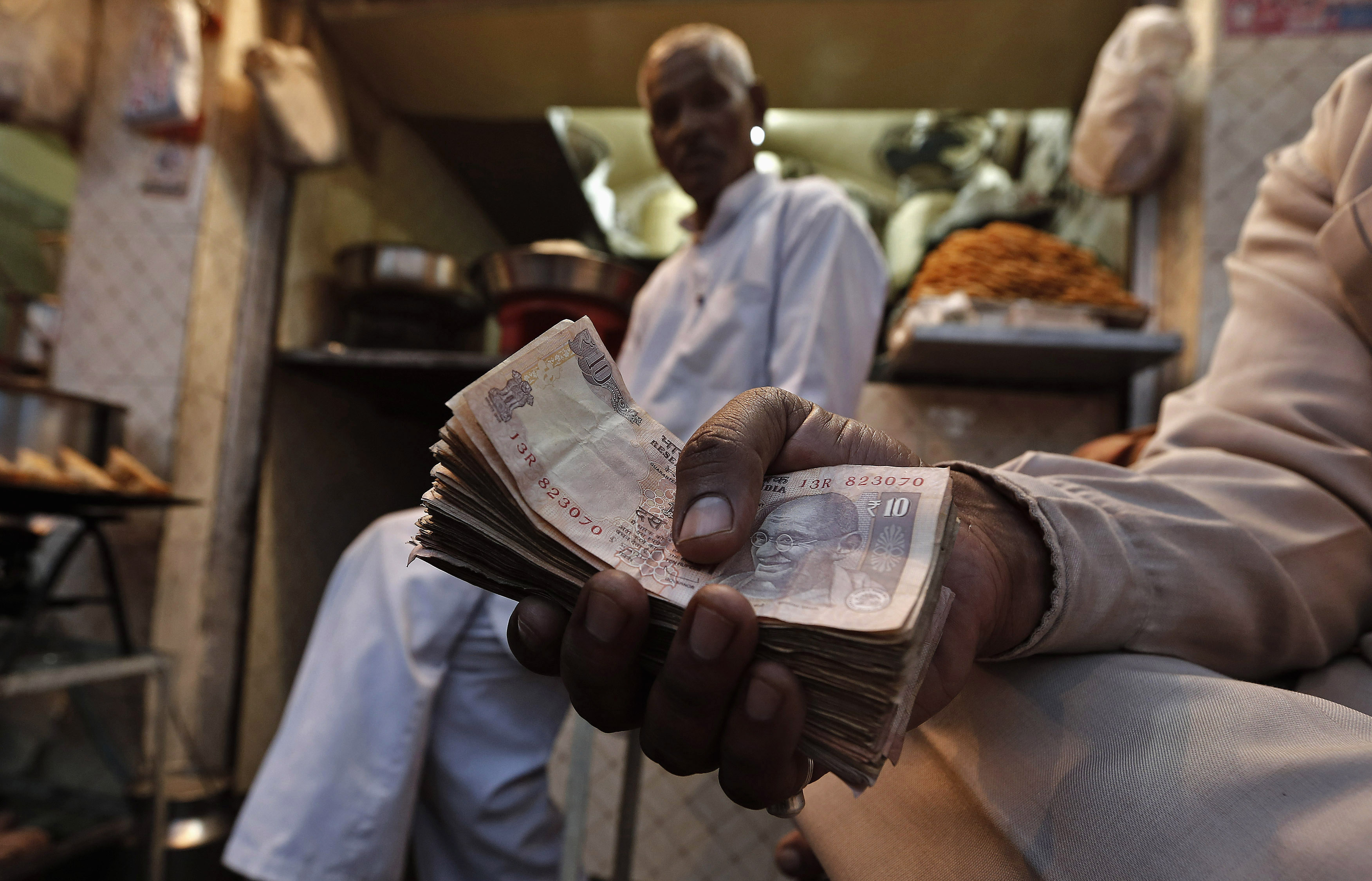 A street side restaurant owner holds a bundle of Indian currency notes as he sits outside his restaurant in New Delhi