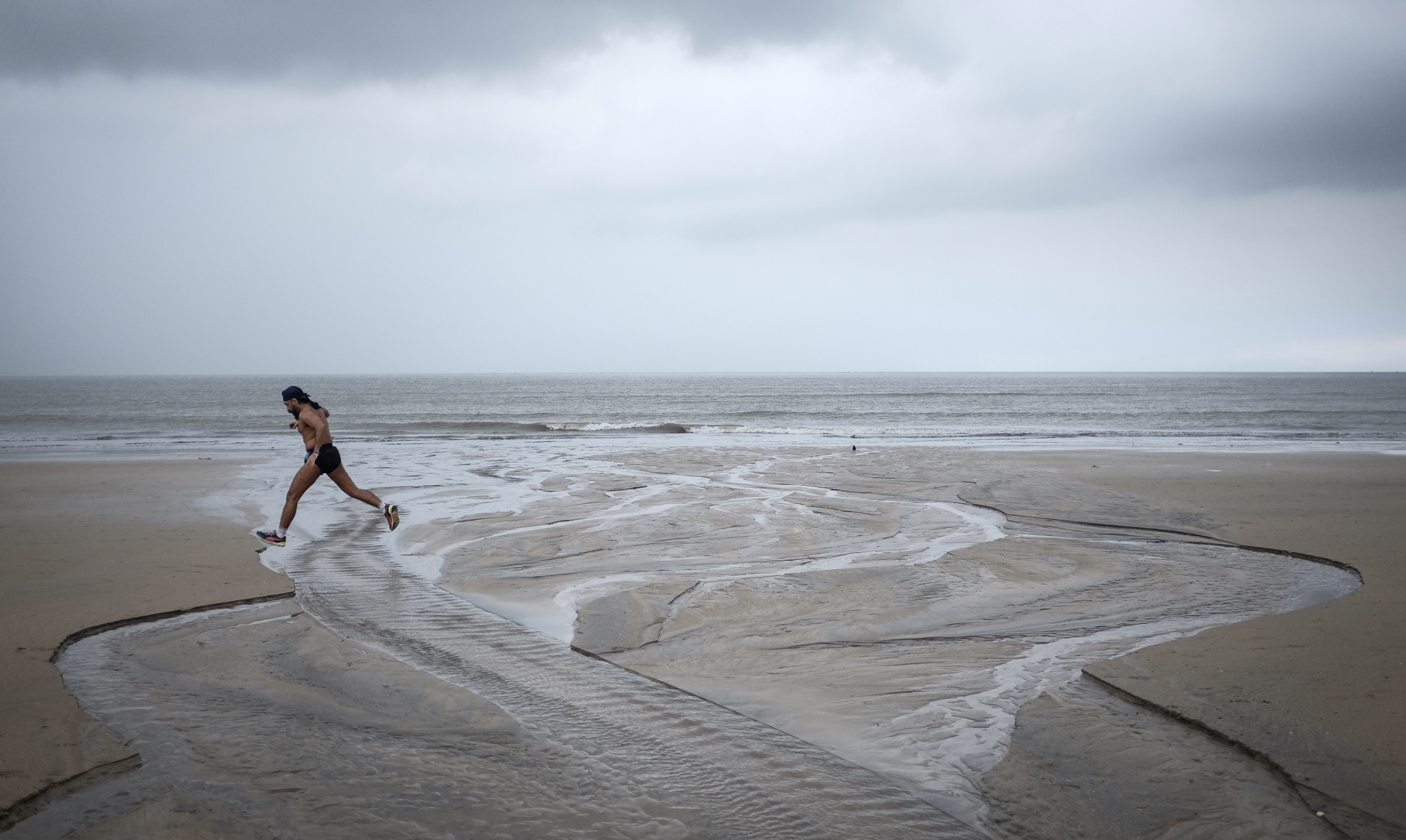 A man runs on a beach along the Arabian Sea against the backdrop of monsoon clouds in Mumbai