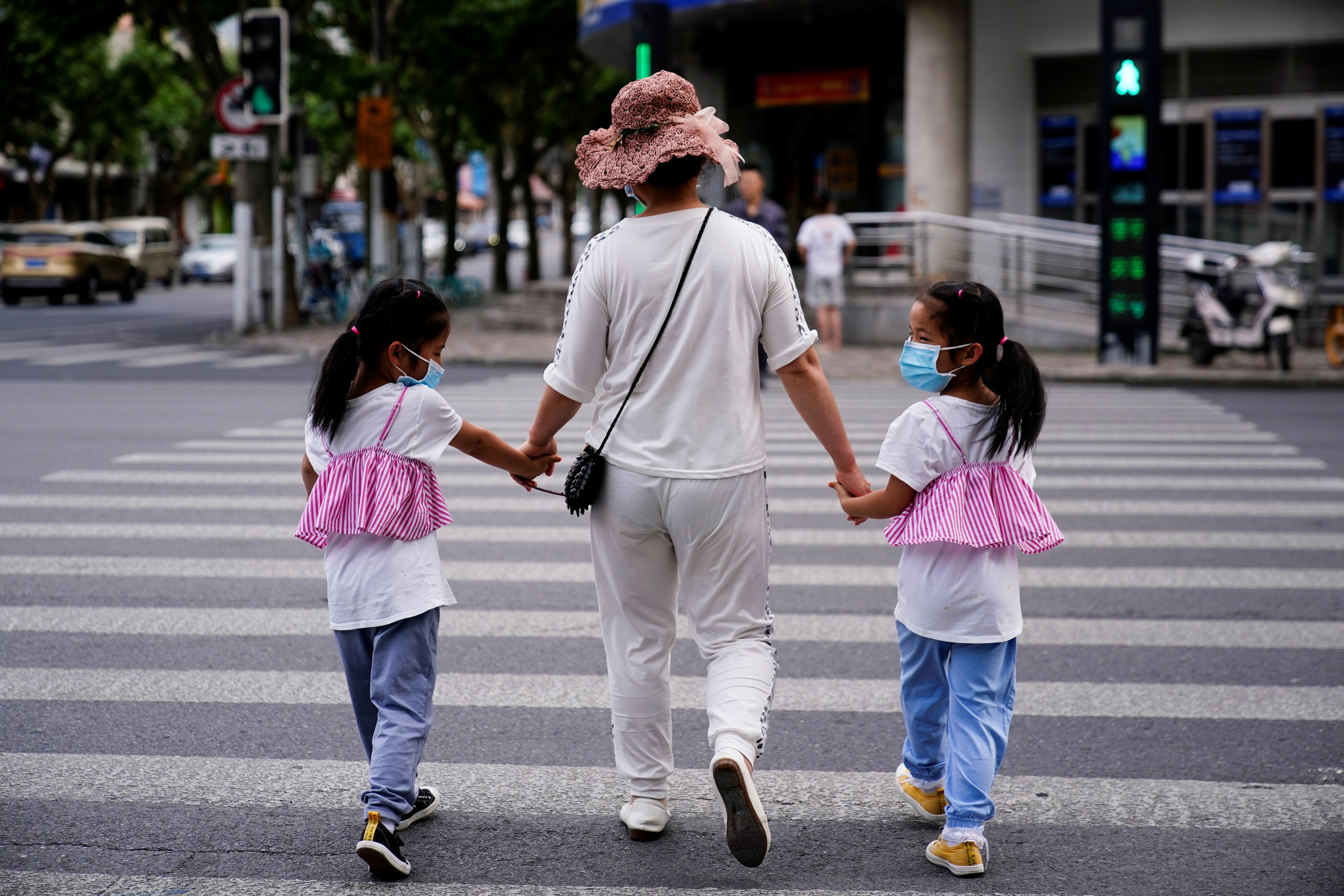 A mother walks with her twin daughters on a street in Shanghai