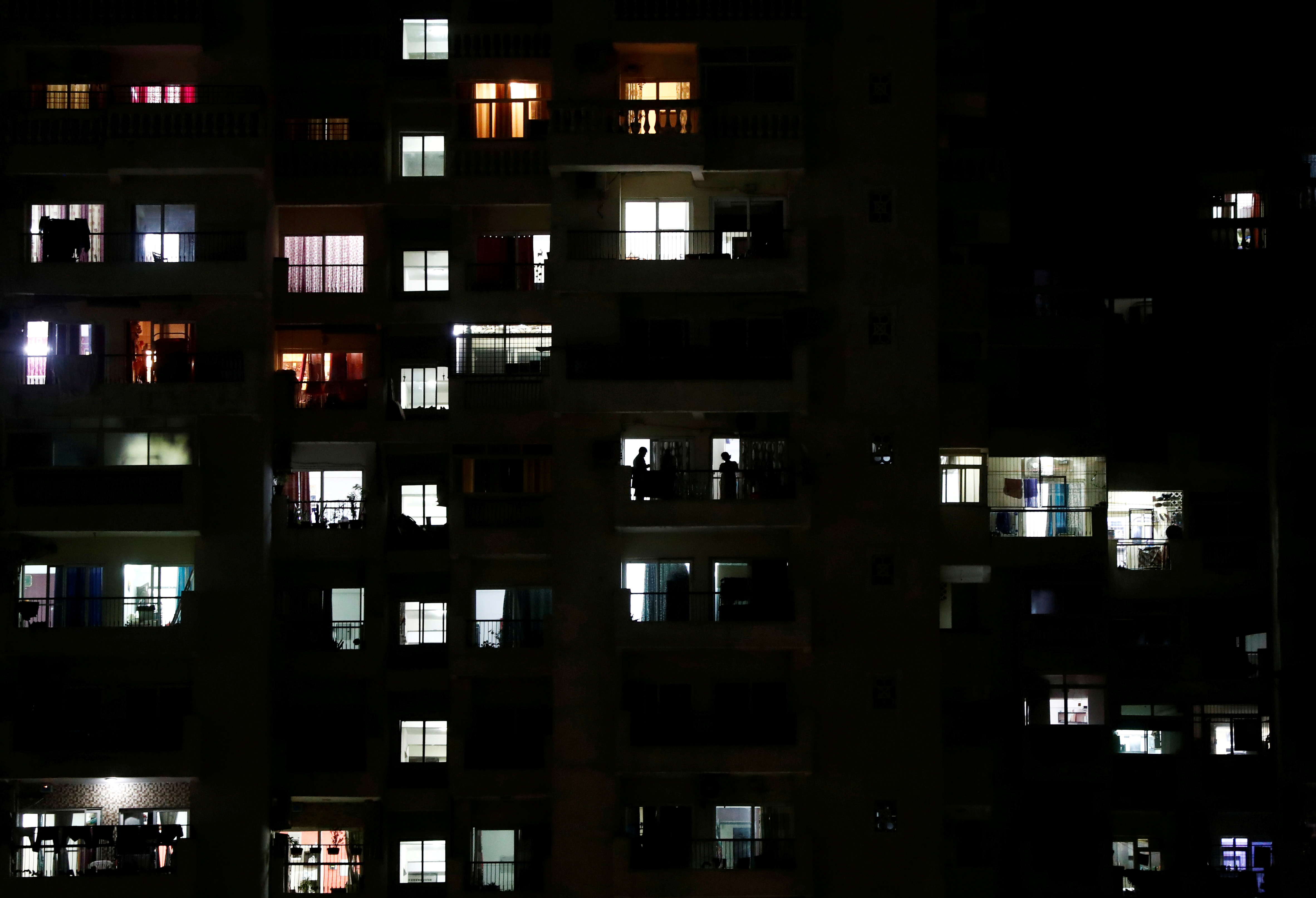 People are silhouetted as they stand in the balconies during a 21-day nationwide lockdown to slow the spreading of the coronavirus disease (COVID-19), in Noida, on the outskirts of New Delhi, India, April 5, 2020. REUTERS/Adnan Abidi/File Photo