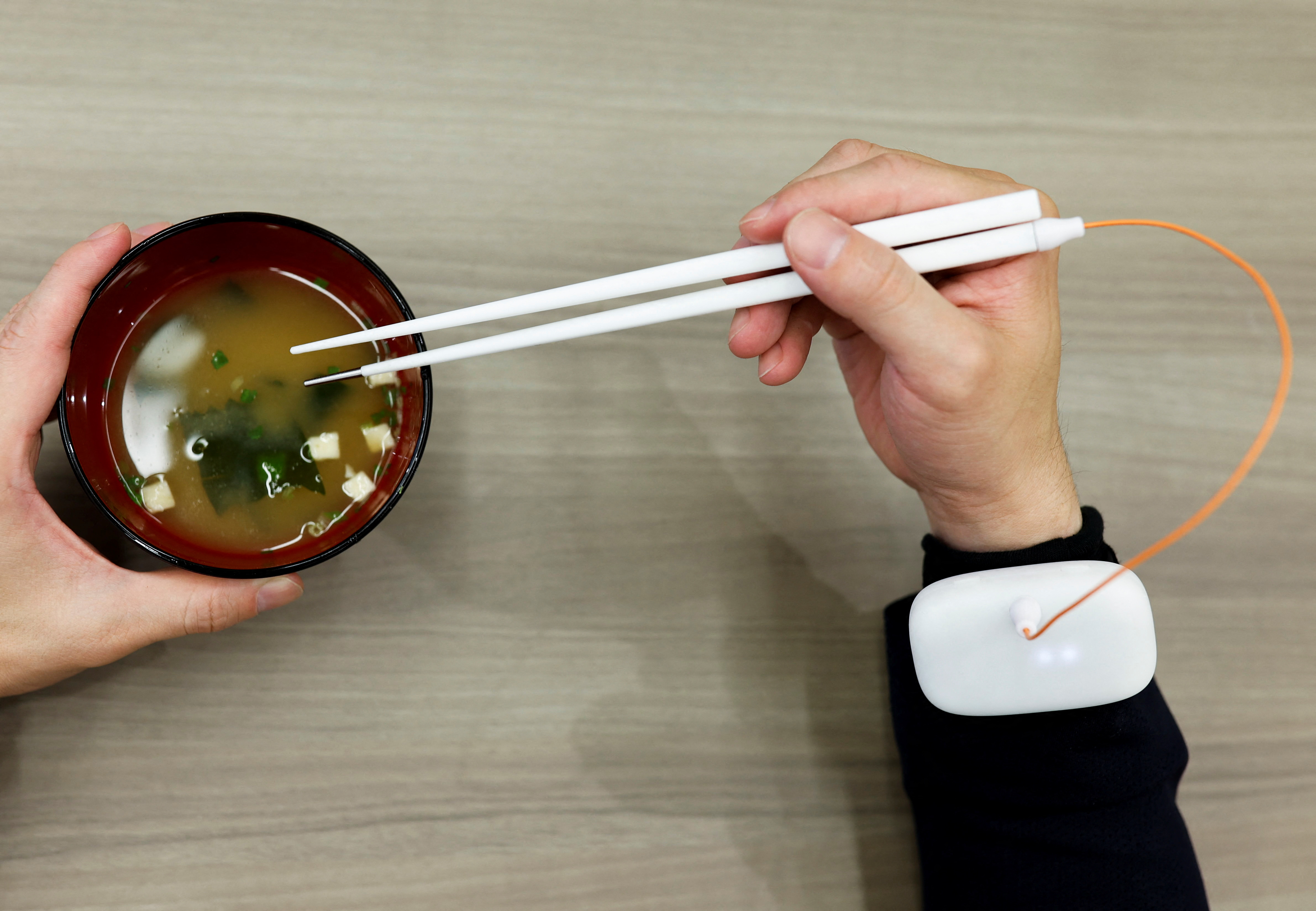 An employee of Kirin Holdings demonstrates chopsticks that can enchance food taste using an electrical stimulation waveform in Tokyo