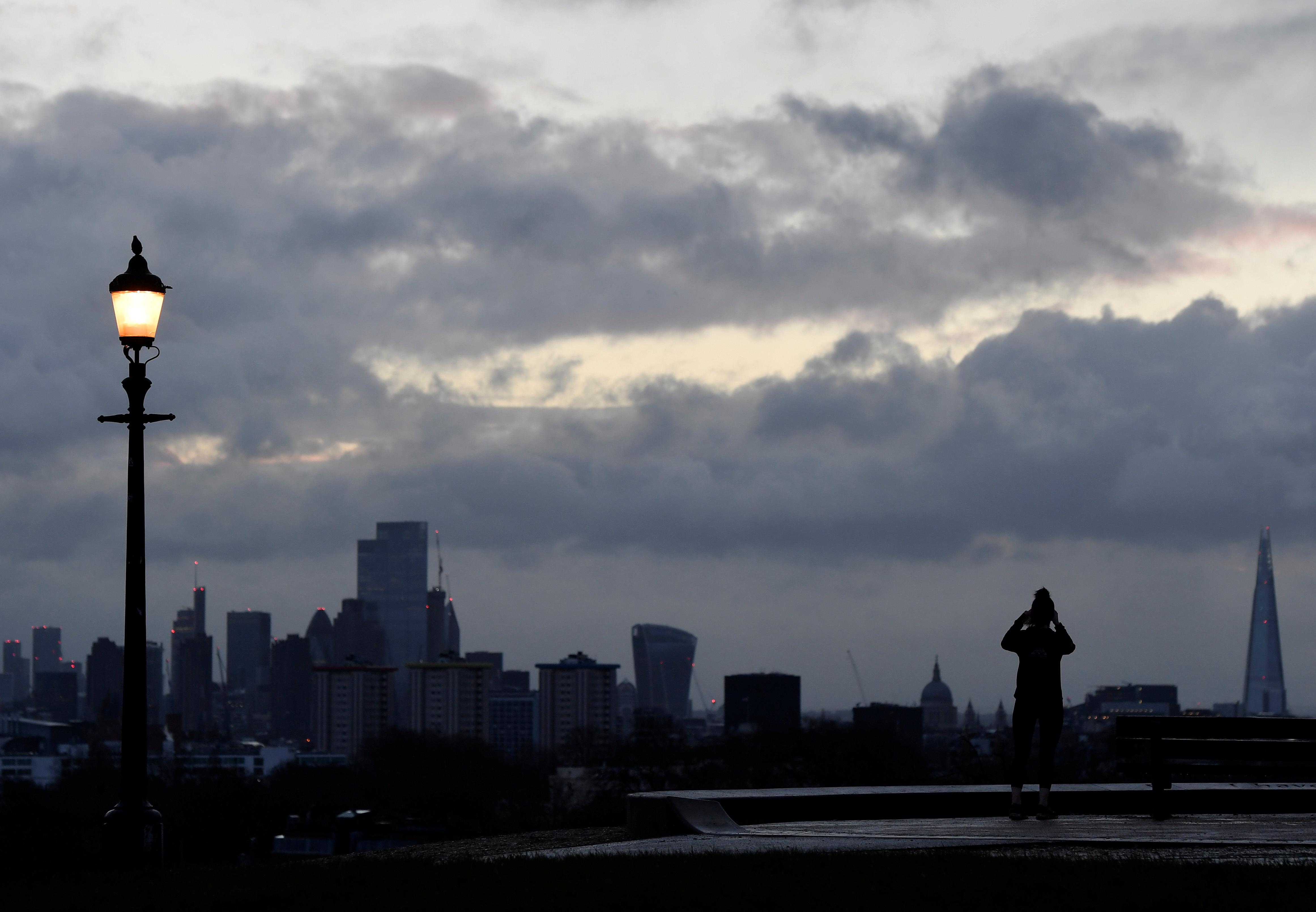 A person takes images of the city skyline at dawn from Primrose Hill, London