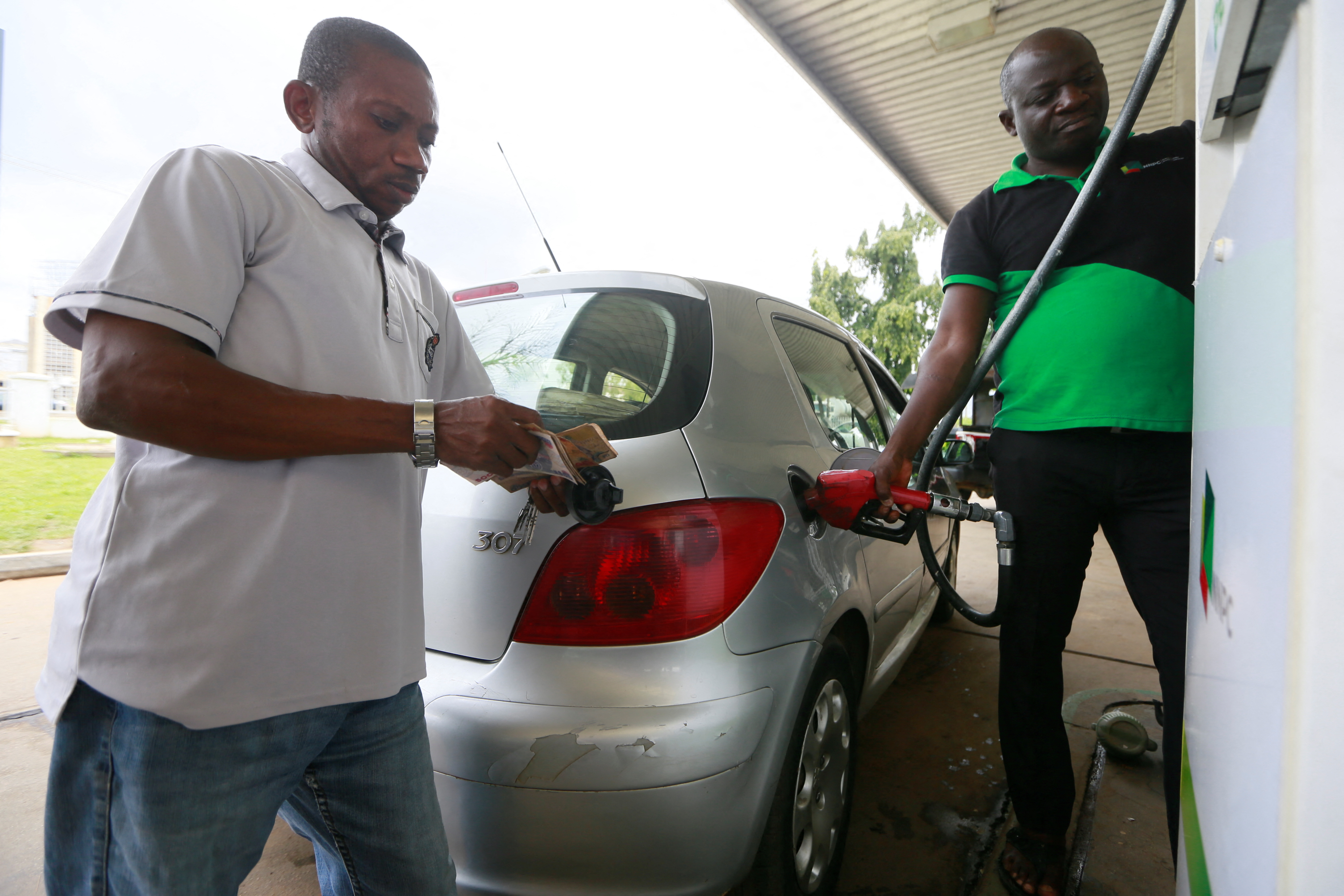 A man counts his money as a petrol attendant fuels his car at the NNPC retail petrol station in Abuja