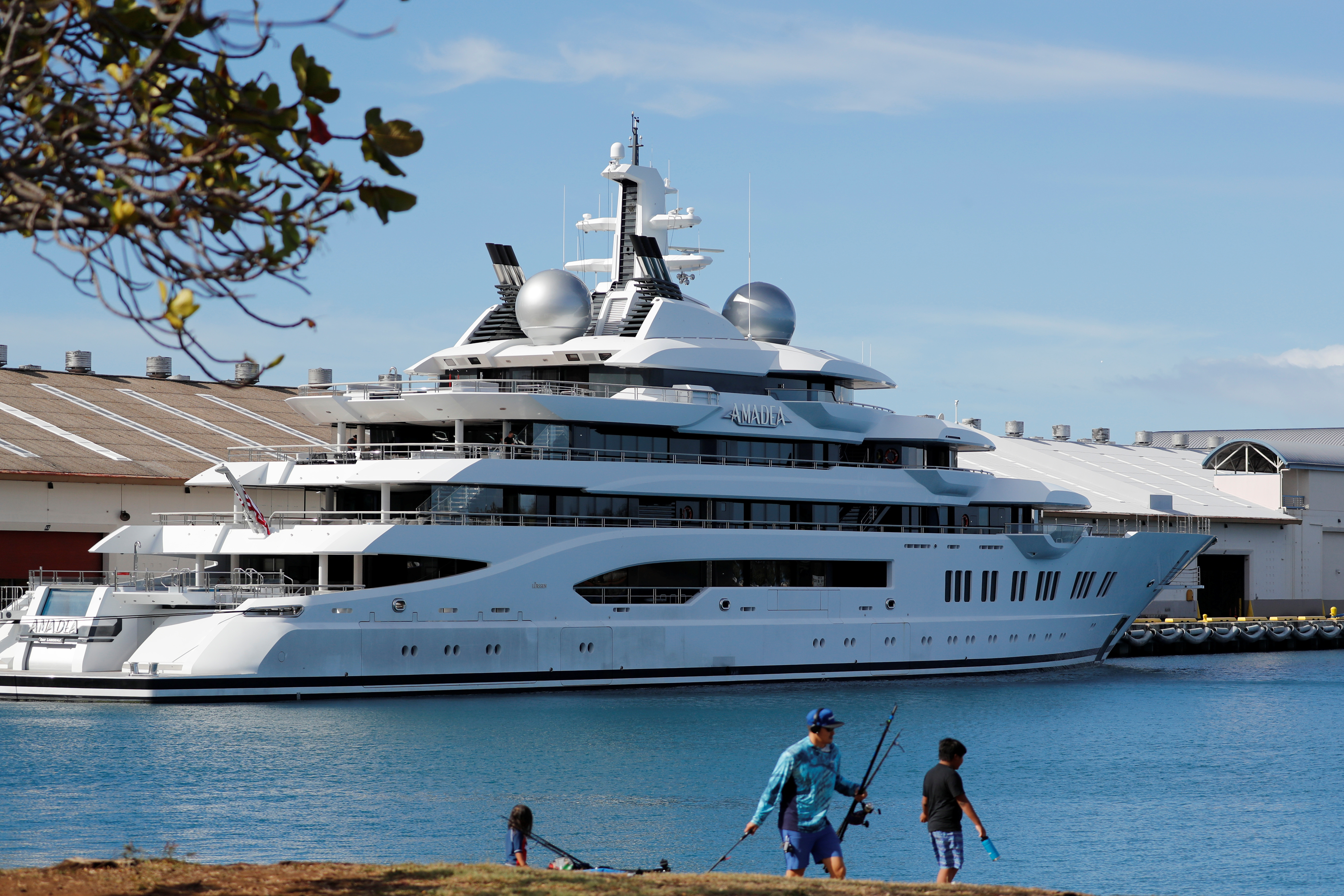 Fishermen set up their gear across the harbor from the Russian-owned super yacht Amadea seized in Fiji by American law enforcement, in Honolulu