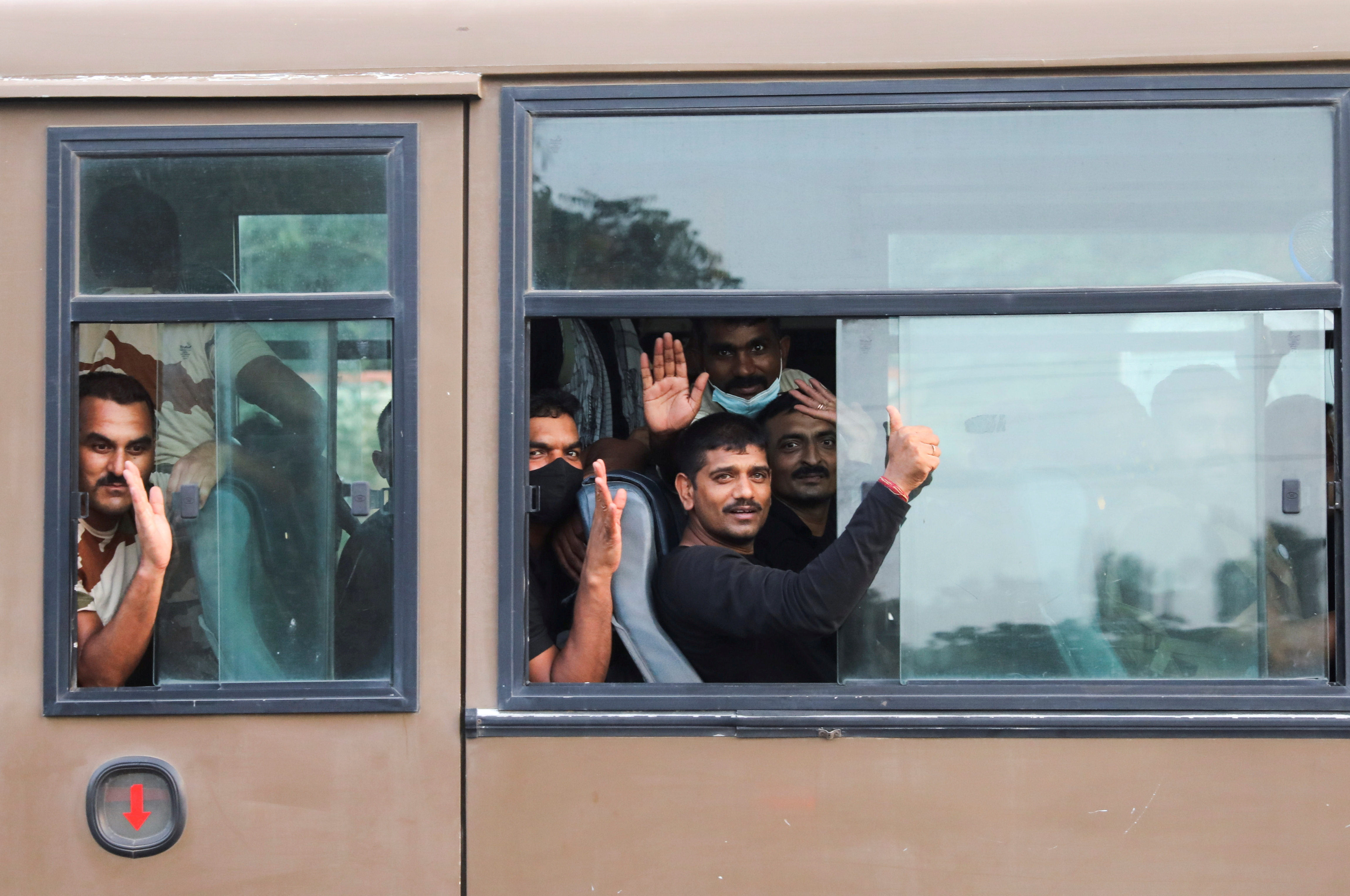 People who were evacuated from Kabul wave from inside the Indo-Tibetan Border Police (ITBP) bus as it leaves the Hindon Air Force Station in Ghaziabad