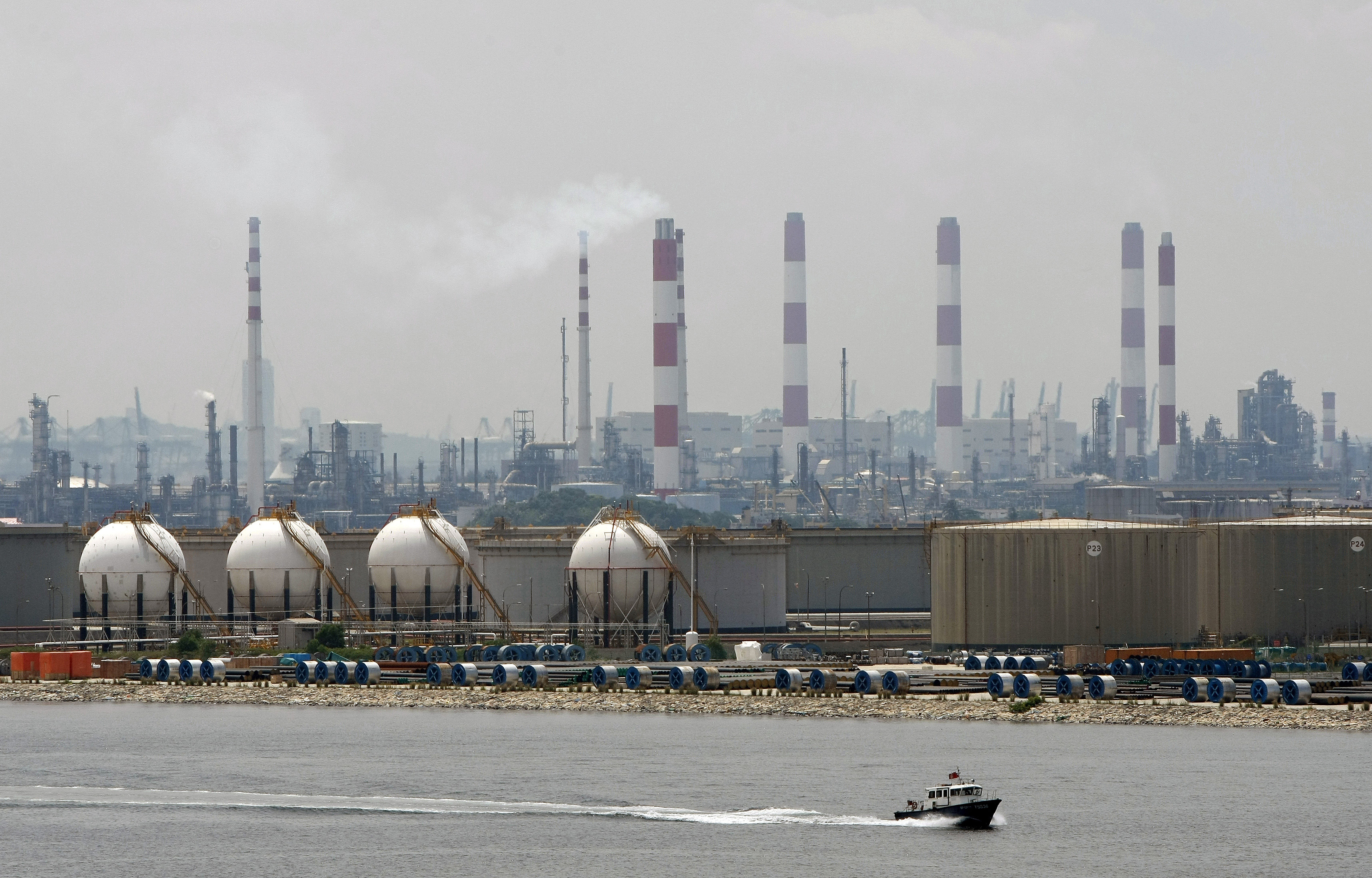 A boat passes in front of an oil refinery located on Singapore's Jurong Island