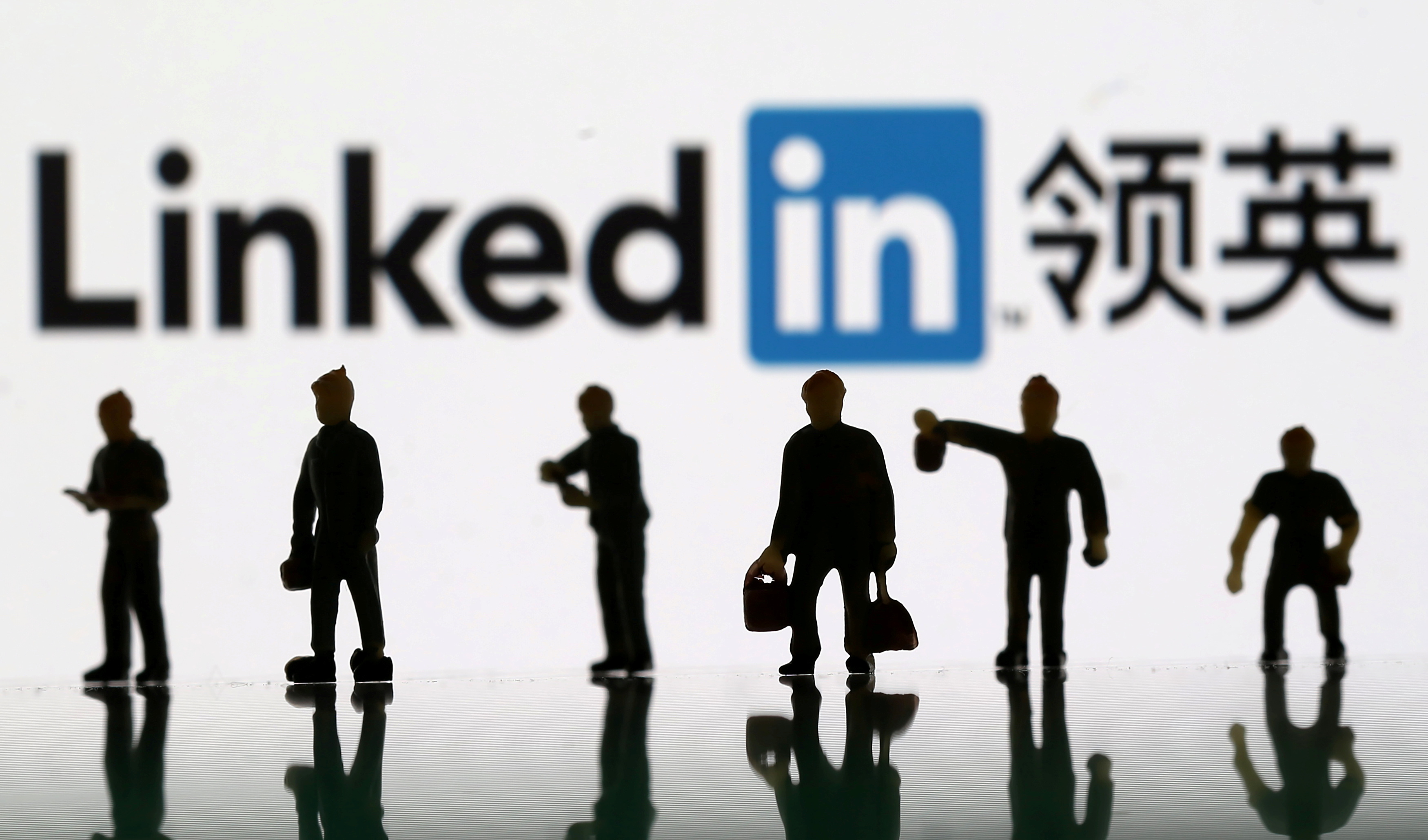 Small toy figures are seen between displayed U.S. flag and Linkedin logo in this illustration picture, August 30, 2018.  REUTERS/Dado Ruvic/Illustration