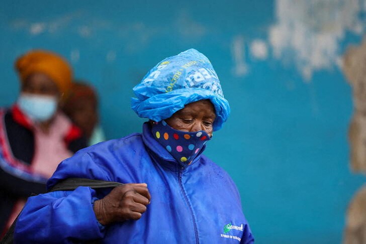 A woman wearing a protective face mask against the COVID-19 and a plastic bag on her head to protect from the rain looks on, as the new Omicron coronavirus variant spreads, at Tsomo
