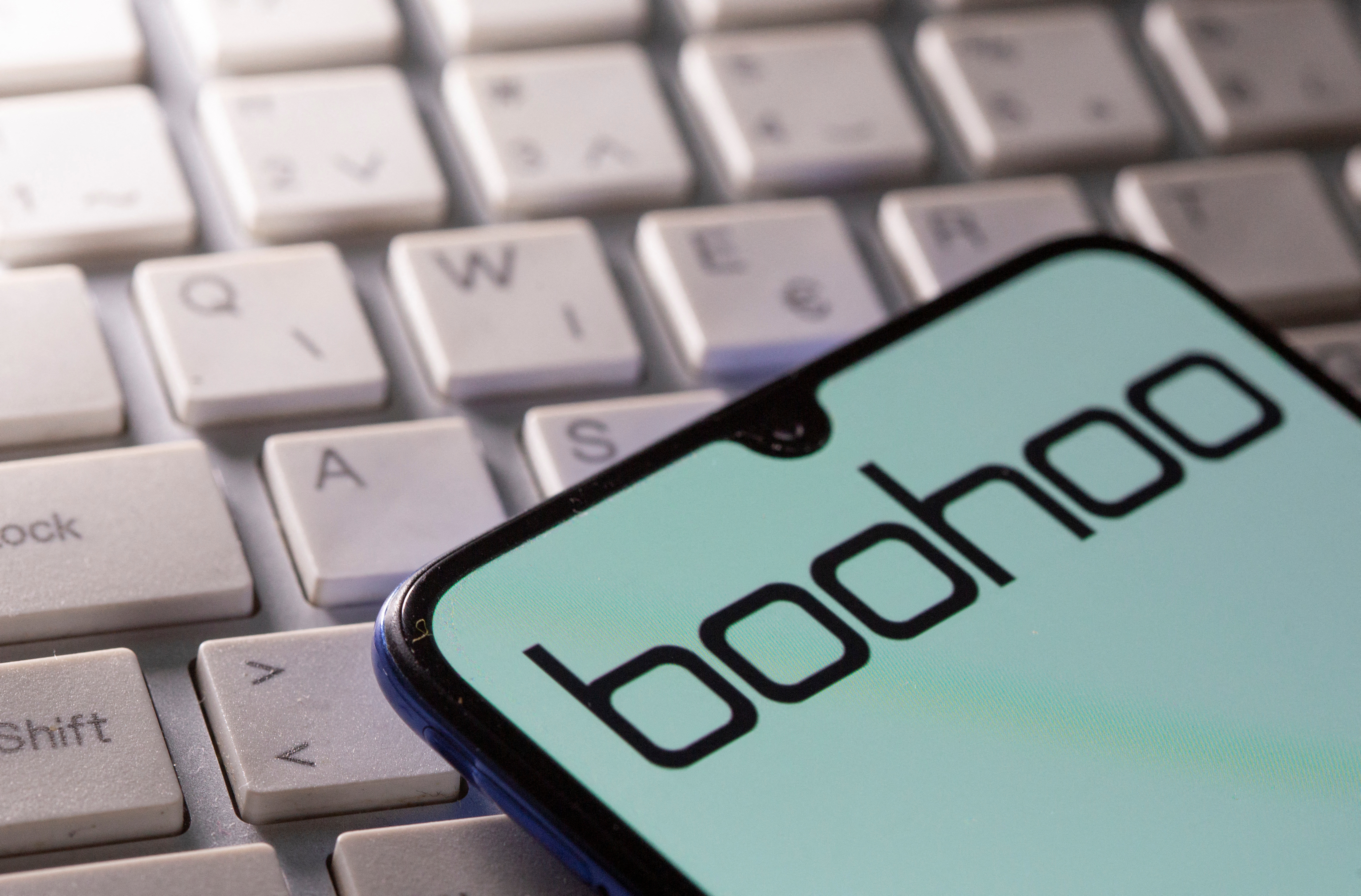A smartphone with the Boohoo logo displayed is seen on a keyboard in this illustration