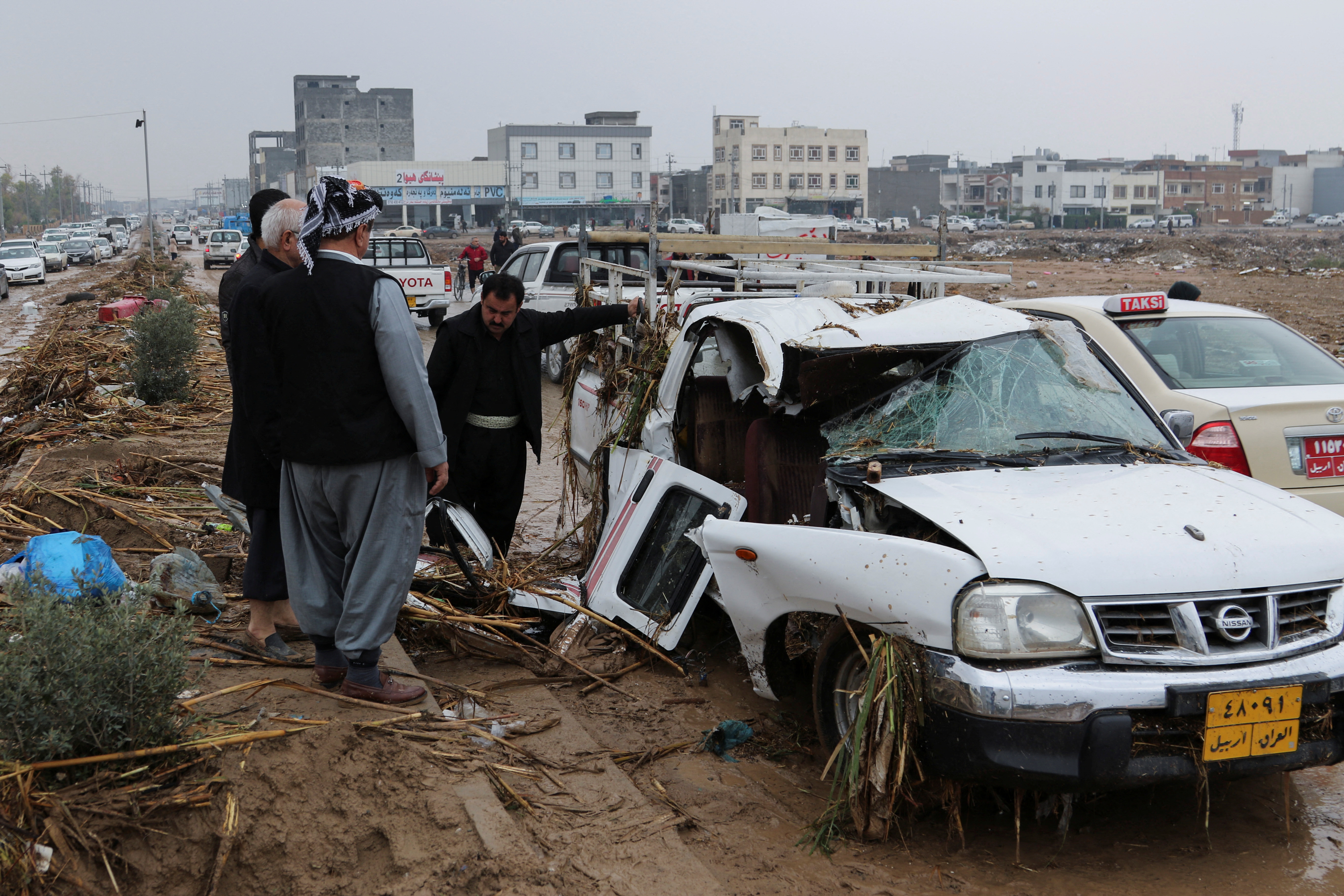 Residents look at a destroyed car after heavy rainfall in Erbil