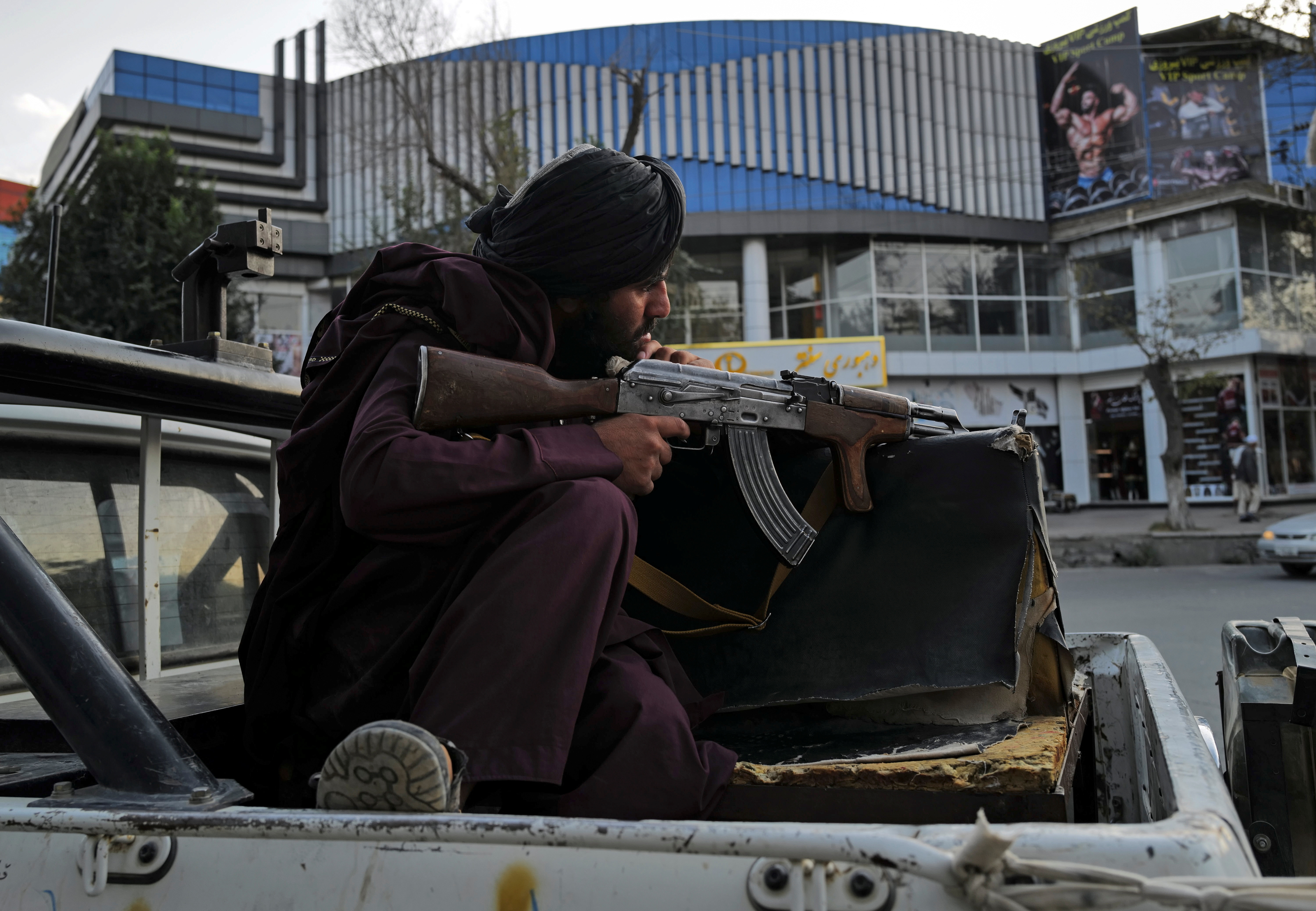 A Taliban fighter sits guard on a vehicle  while his comrades are praying at Deh Bori square in Kabul,