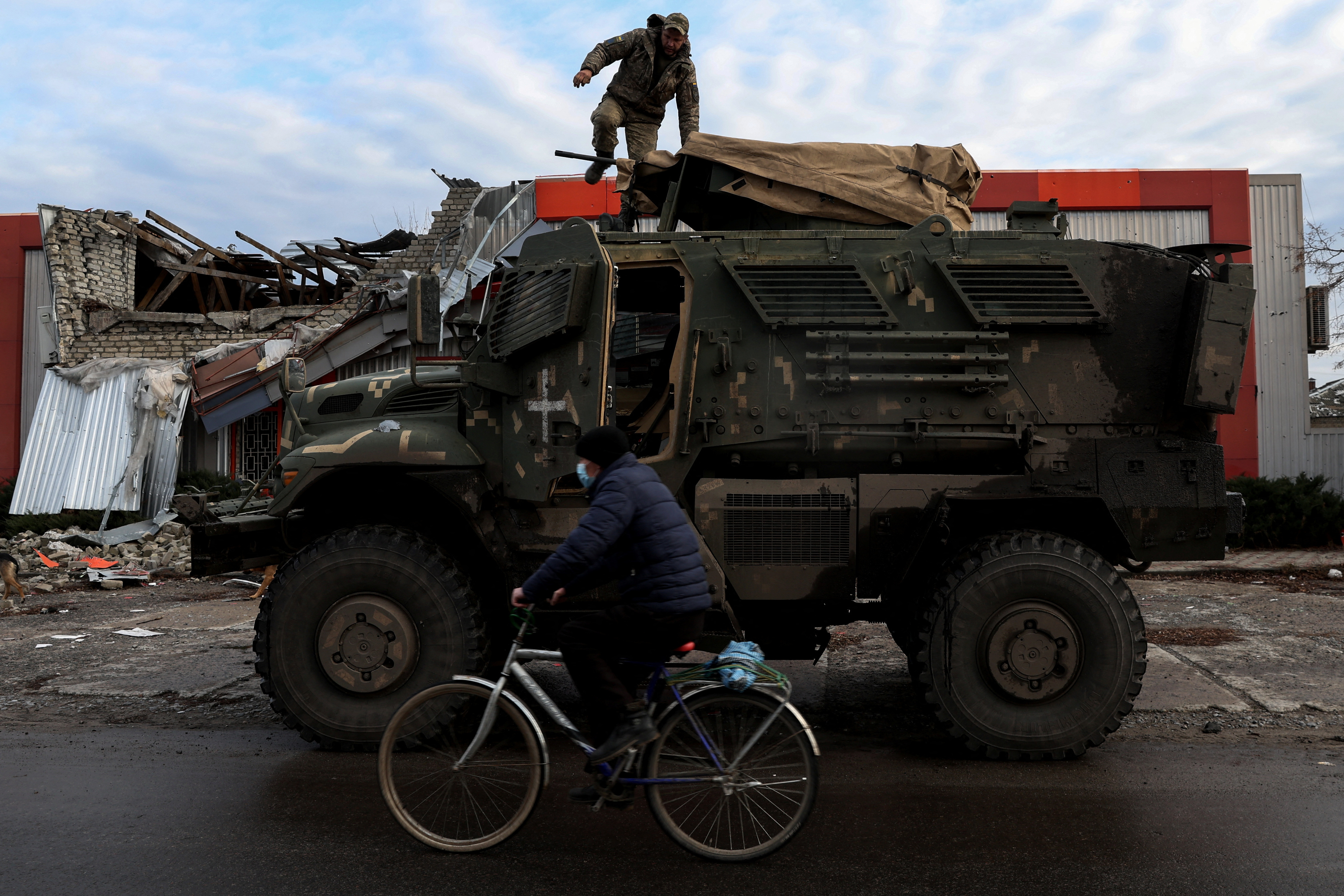 जैसा कि यूक्रेन पर रूस का आक्रमण जारी है, यूक्रेन के डोनेट्स्क क्षेत्र में पूर्व में रूस के कब्जे वाले शहर लाइमैन में एक बाइक सवार एक सुरक्षात्मक मास्क पहने एक व्यक्ति यूएस मैक्सप्रो सैन्य वाहन के ऊपर से एक सैनिक को पार करता है।
